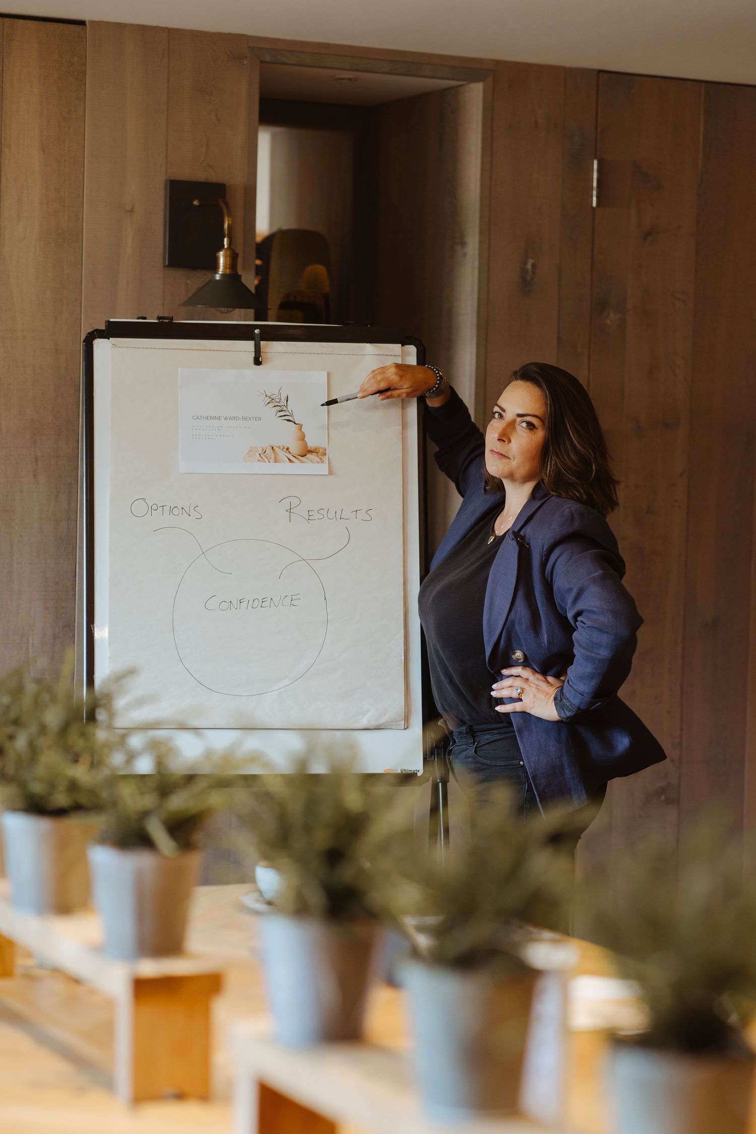 A woman stands confidently by a flip chart, gesturing toward her notes as she leads a presentation.