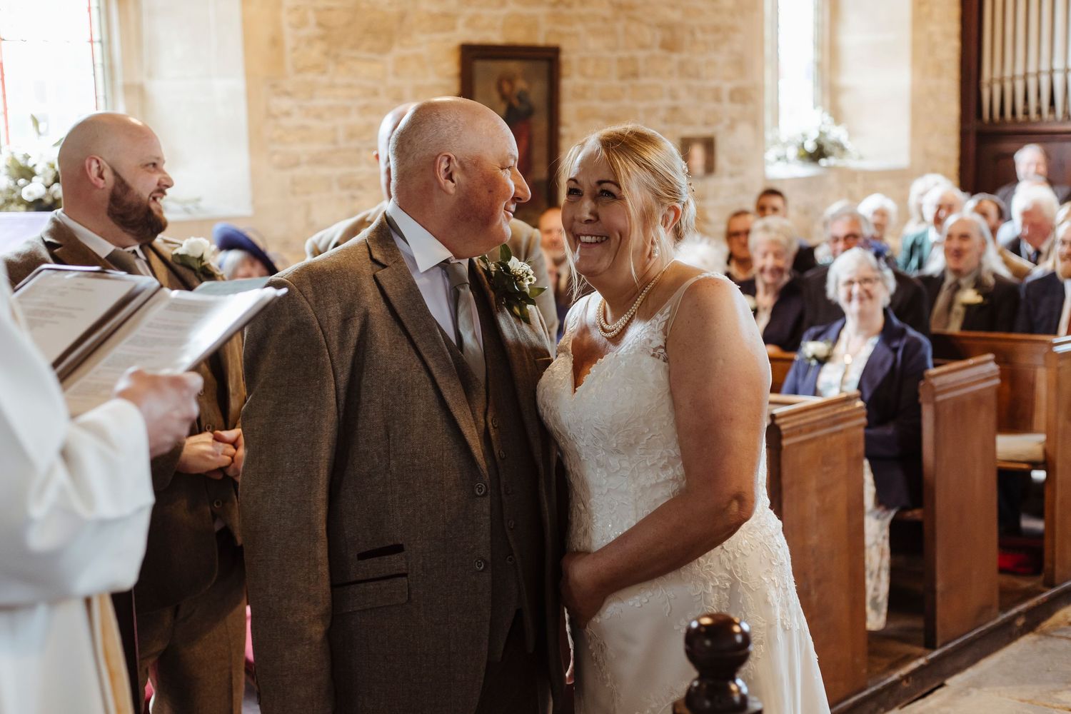The couple shares a warm, joyful glance at the altar as guests look on, filling the moment with love and celebration.