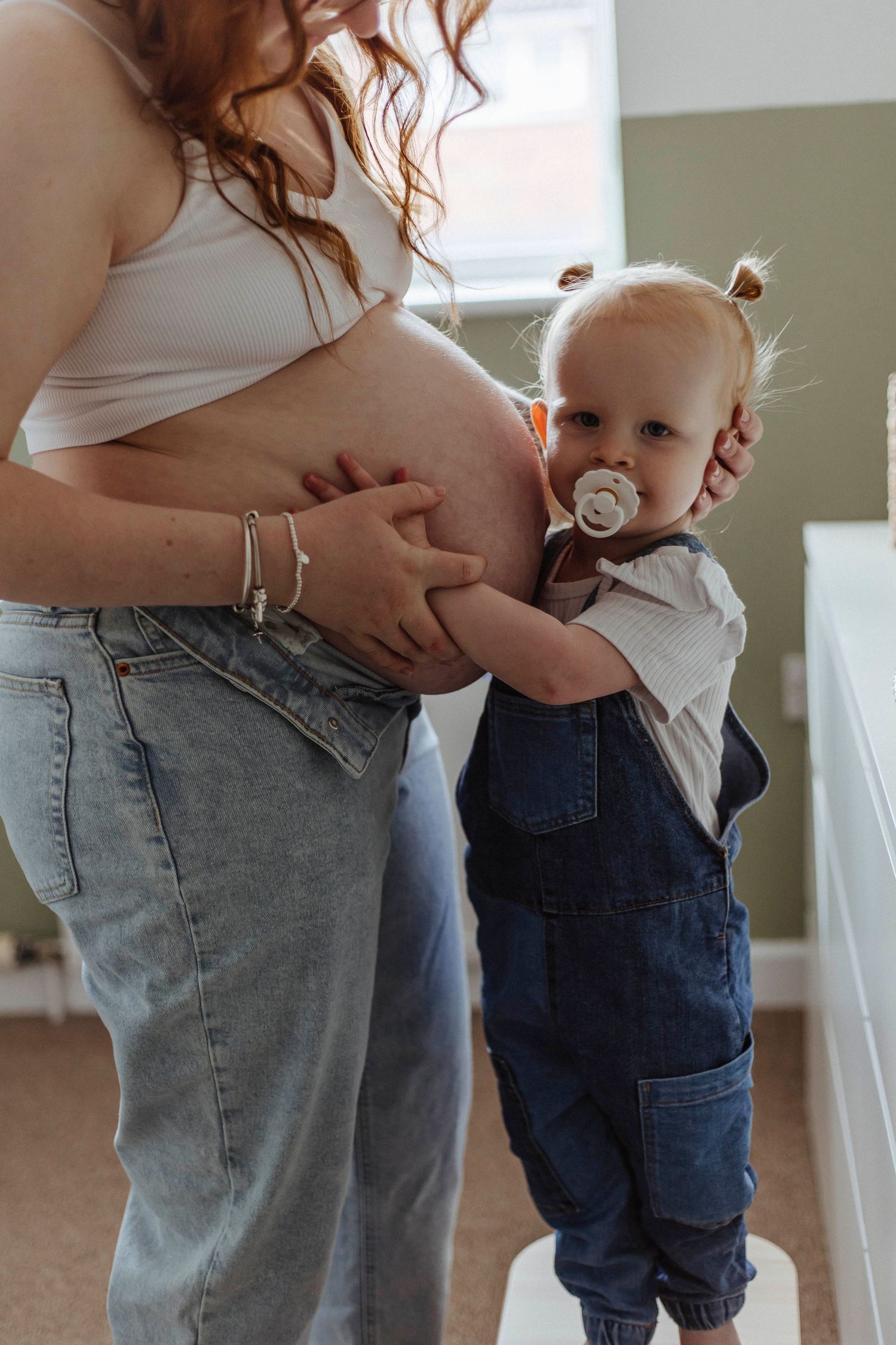 A little one rests a hand on a pregnant belly, sharing a tender, curious moment with their parent.