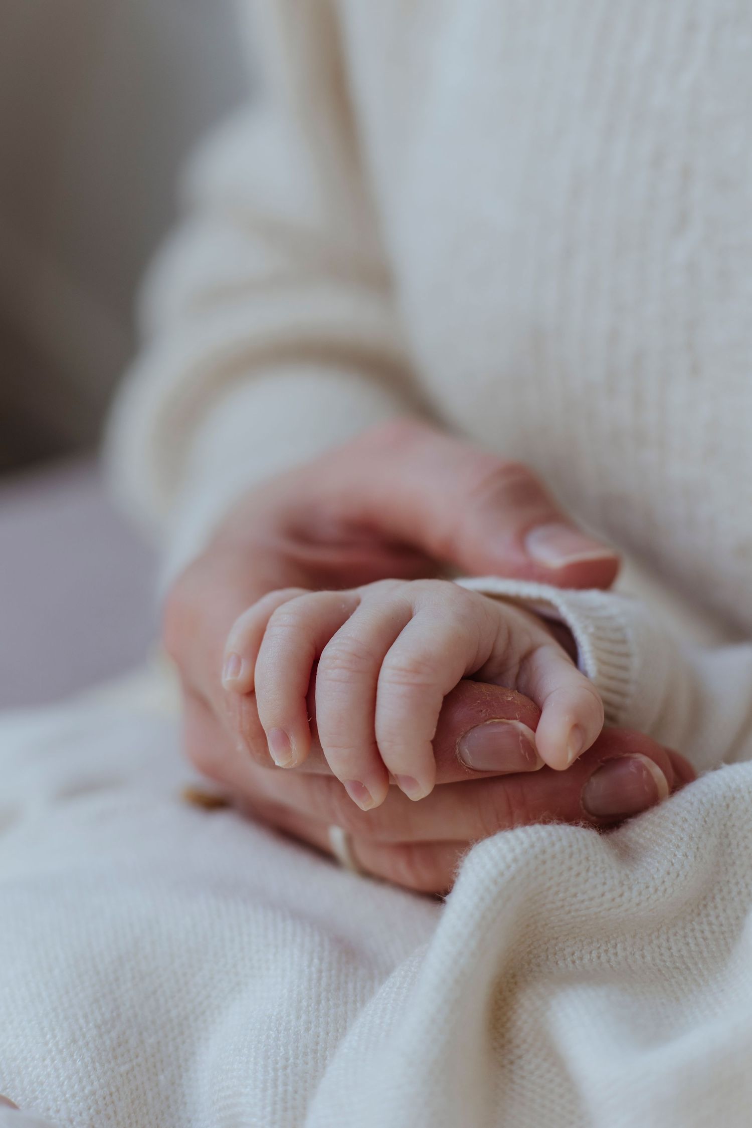 An adult gently holds a newborn’s tiny hand, soft light emphasising the warmth of the moment.