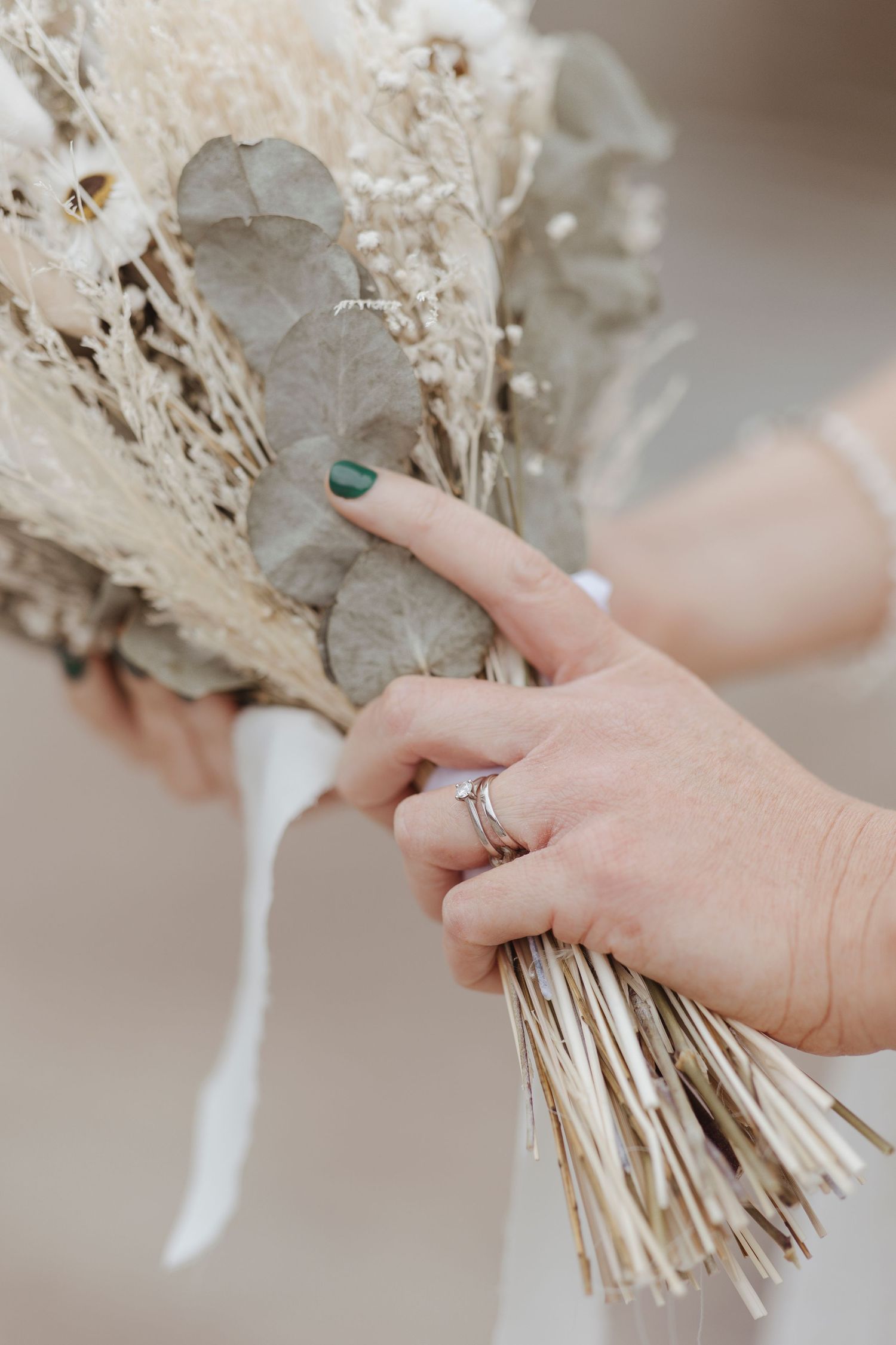 Hands holding a dried floral bouquet, showing rings and green-painted nails.