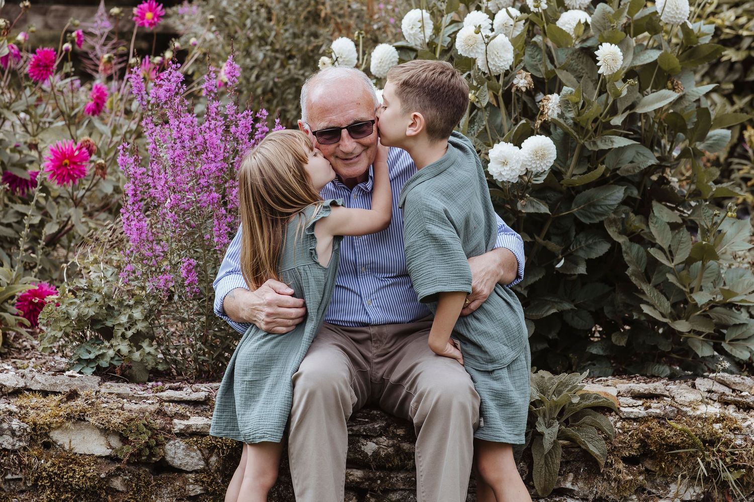 grandfather being kissing by granddaughter and grandson on the cheek with blossoming flowers behind them