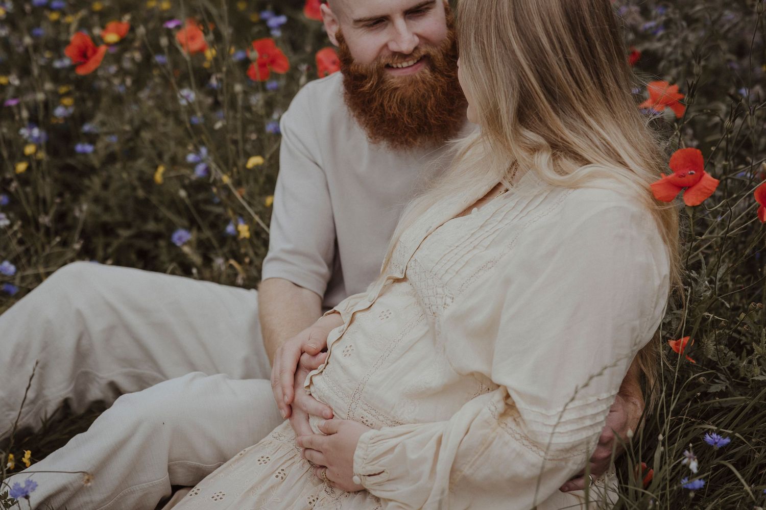 A peaceful field moment as an expecting couple sits together, hands resting lovingly on the baby bump.