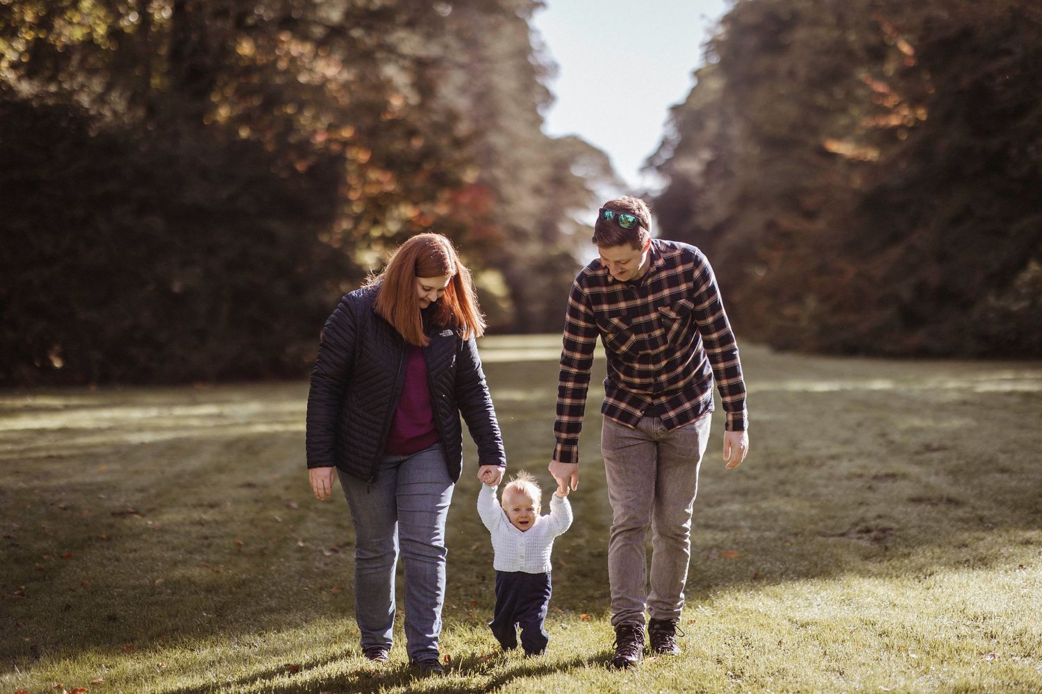 mother father and toddler walking down the path at westonbirt with autumnal trees in the background