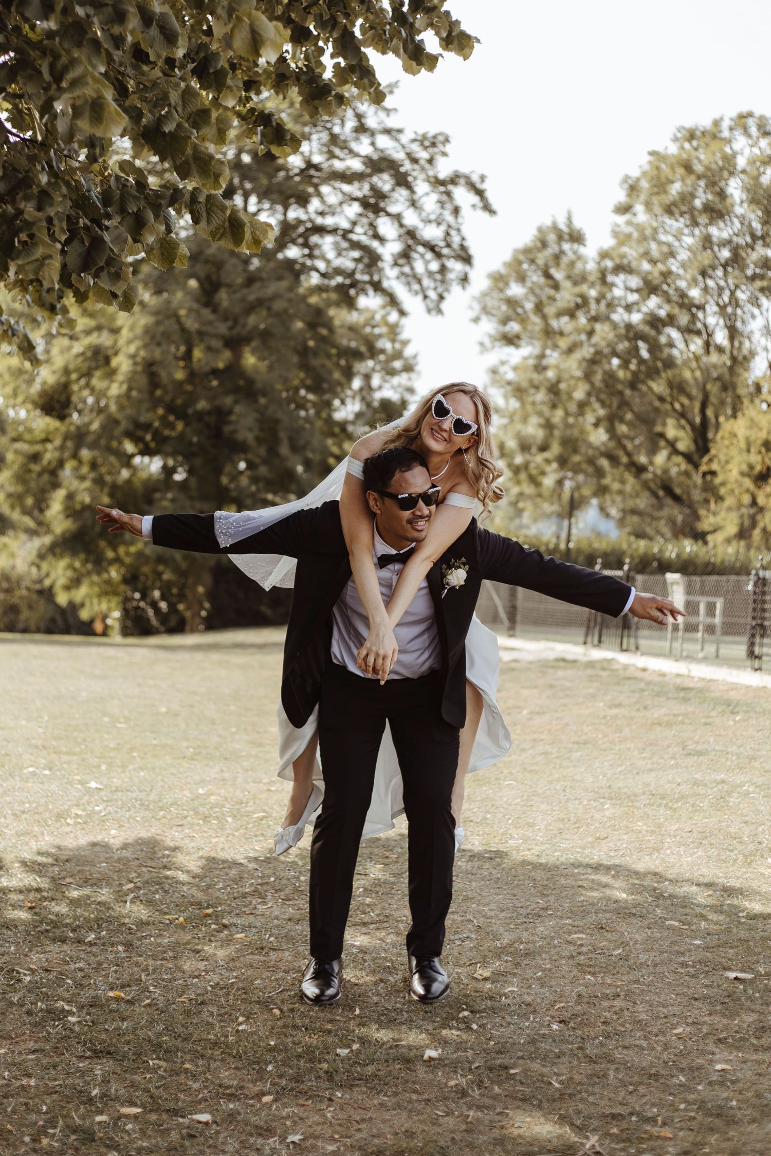 bride on grooms back hugging him in the sunshine