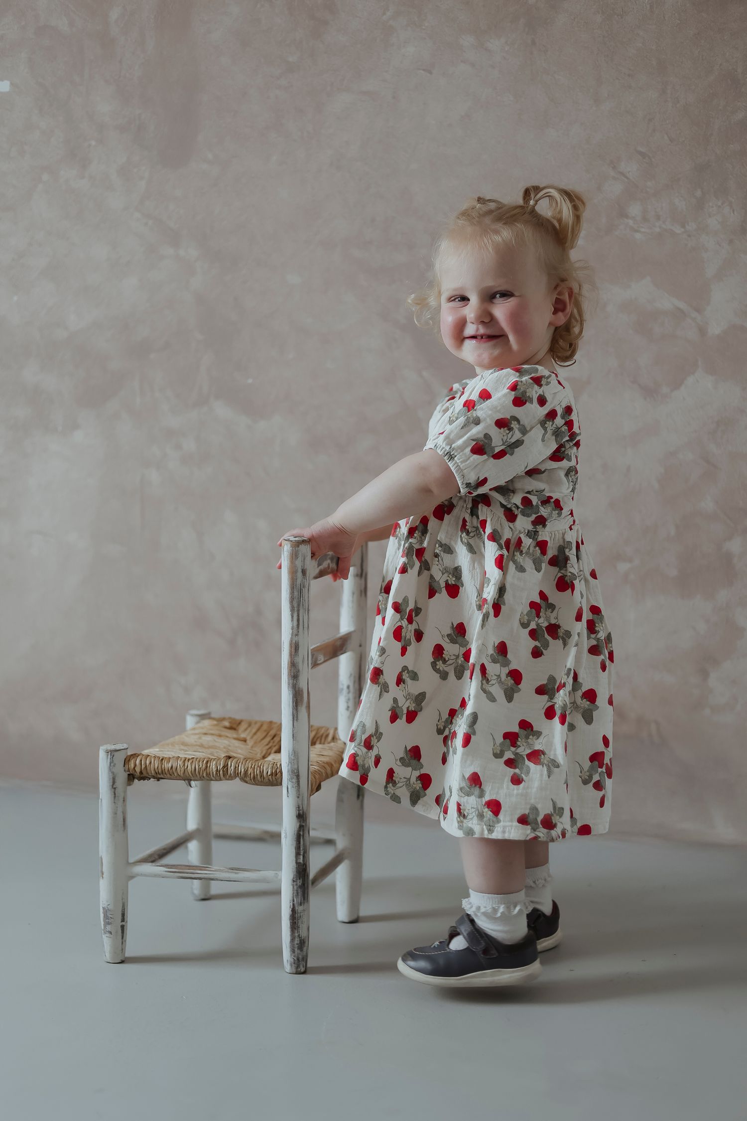 toddler smiling proudly whilst holding onto a chair in the studio