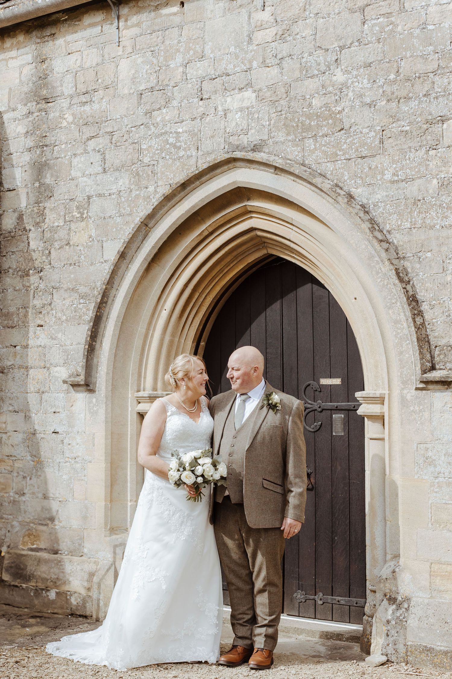 The couple stands closely together at the arched doorway, sharing a warm, contented moment on their wedding day.