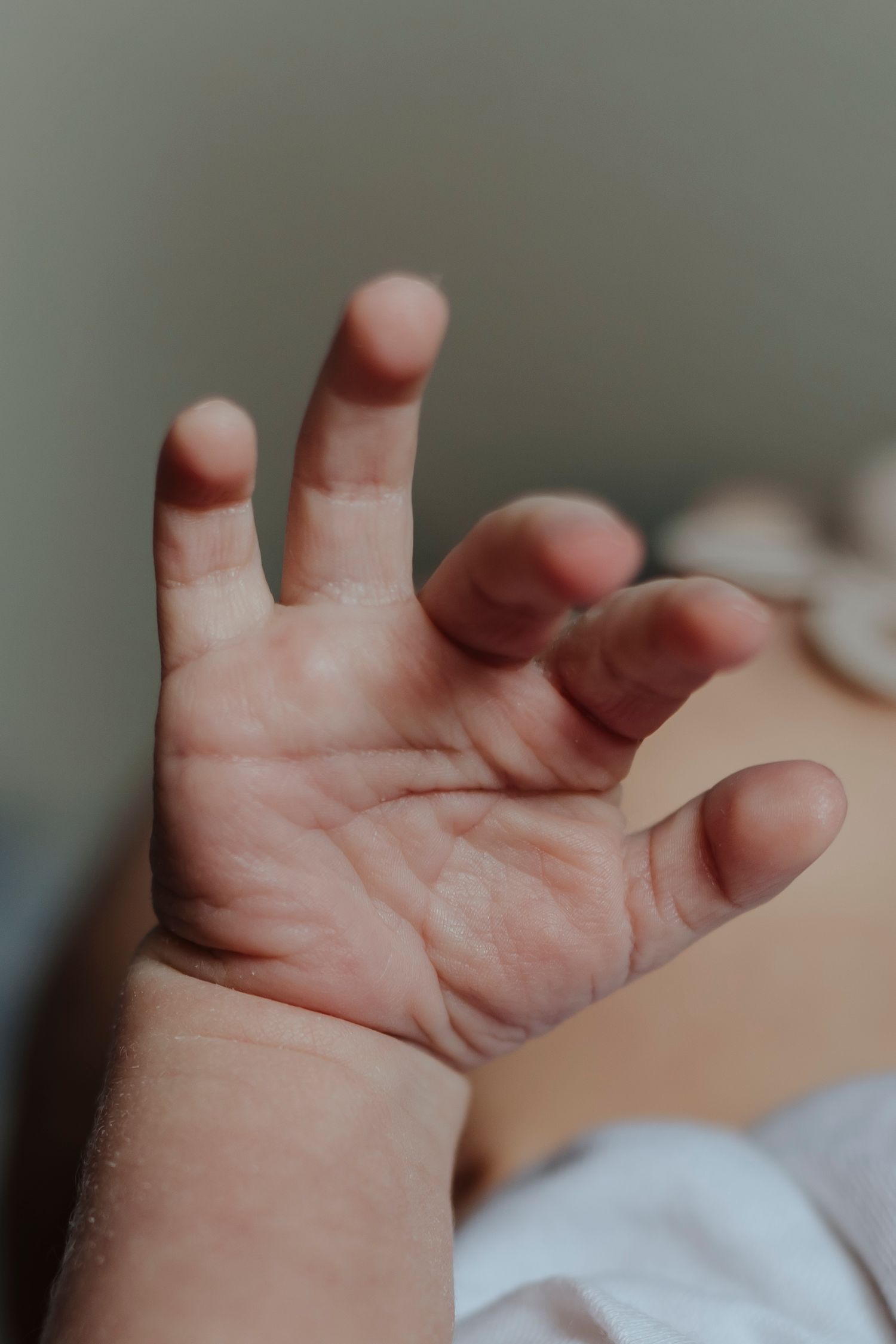 A newborn’s tiny hand stretches open, soft and delicate against a blurred background.