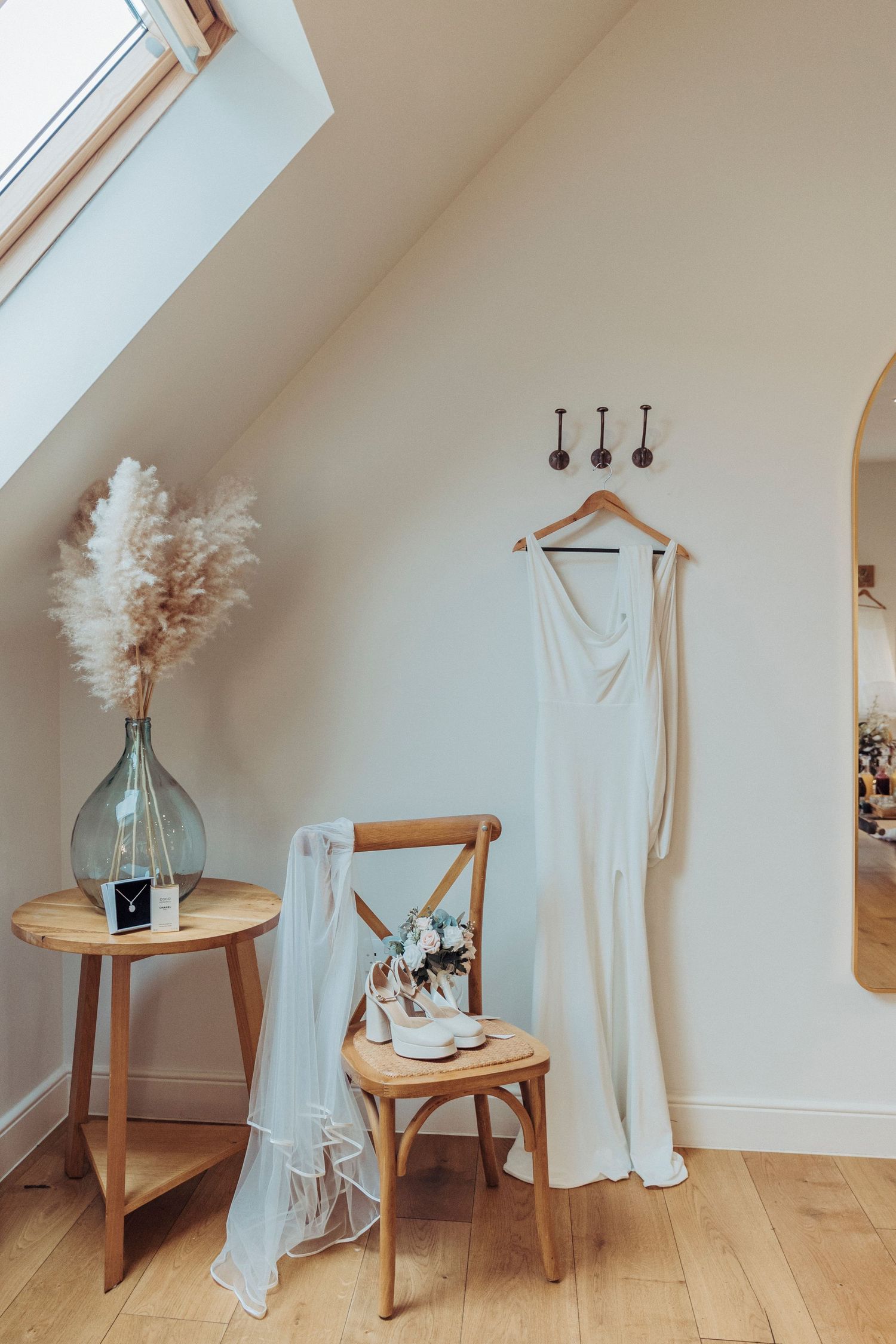 A simple, elegant bridal dress hangs beside a chair adorned with shoes and a veil, ready for the big moment.