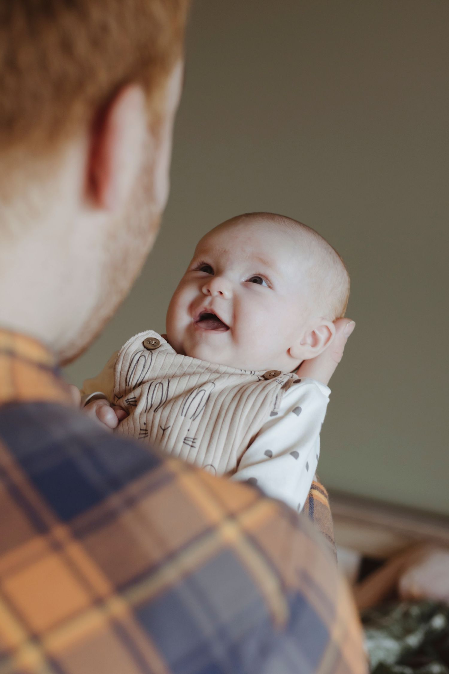 A baby looks up with a bright, happy expression while being held in someone’s arms.