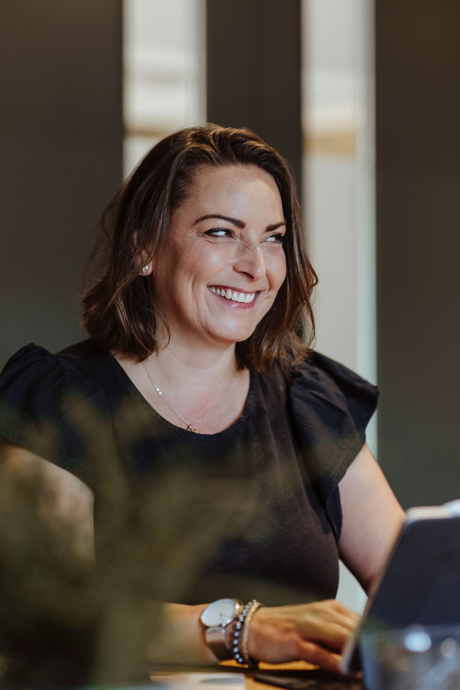 A woman sits at a laptop, smiling warmly as she works.
