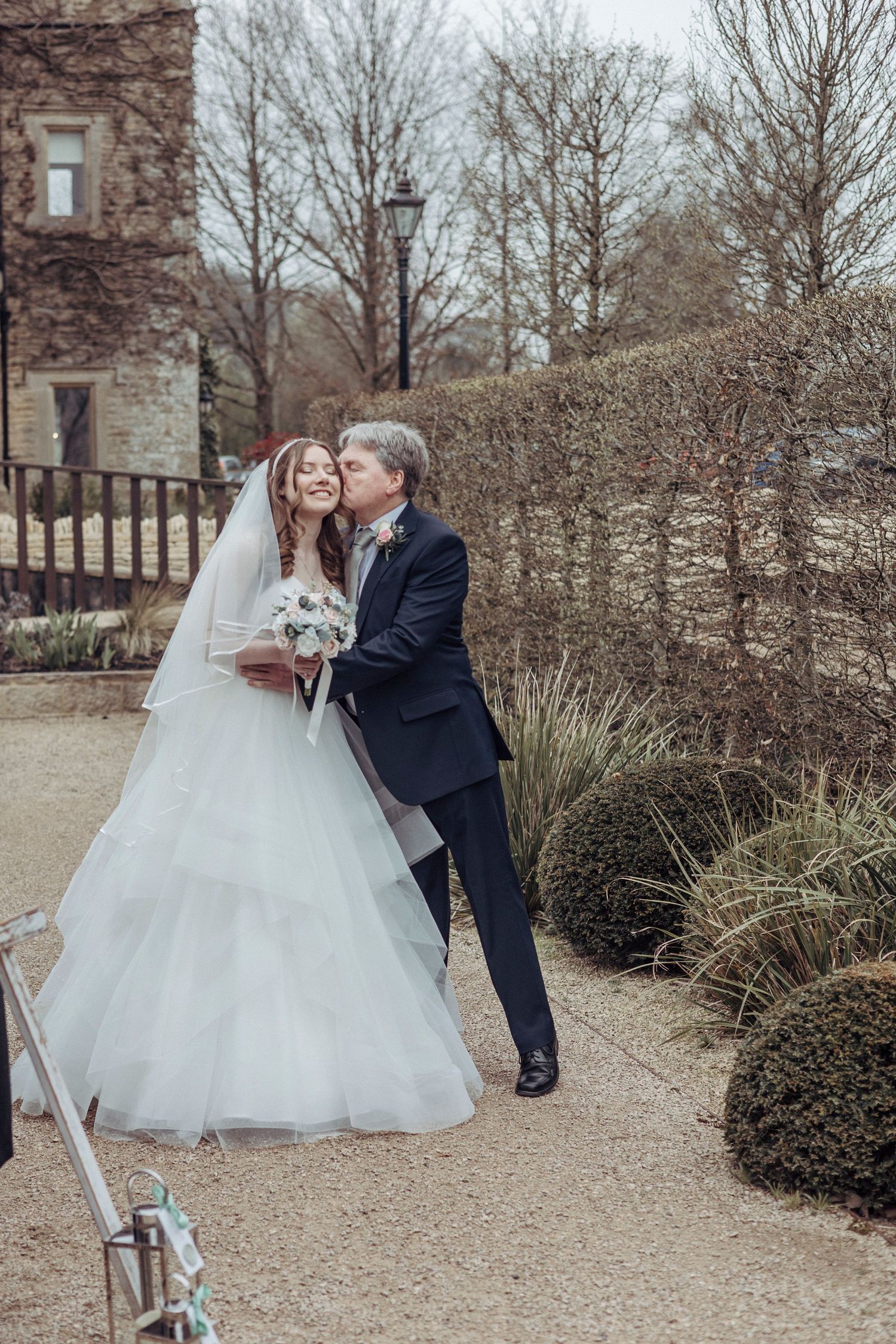 A bride shares a sweet, joyful moment outdoors with an older gentleman, likely a proud family member.