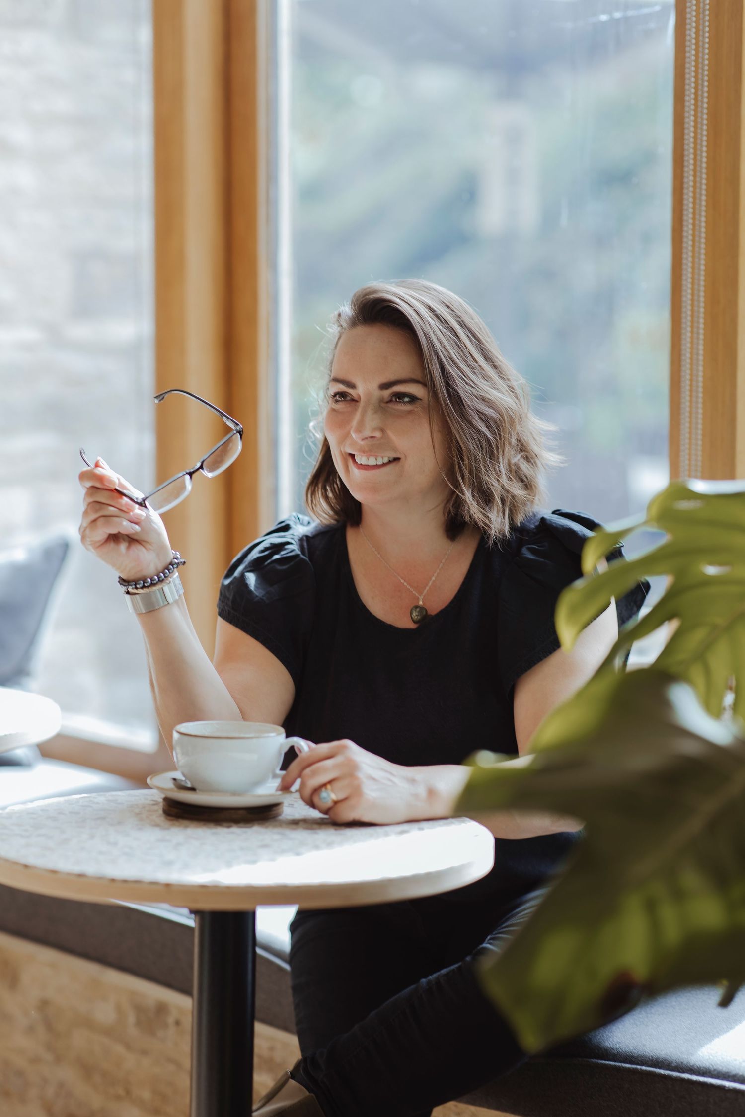 woman sat in cafe holding her glasses looking out