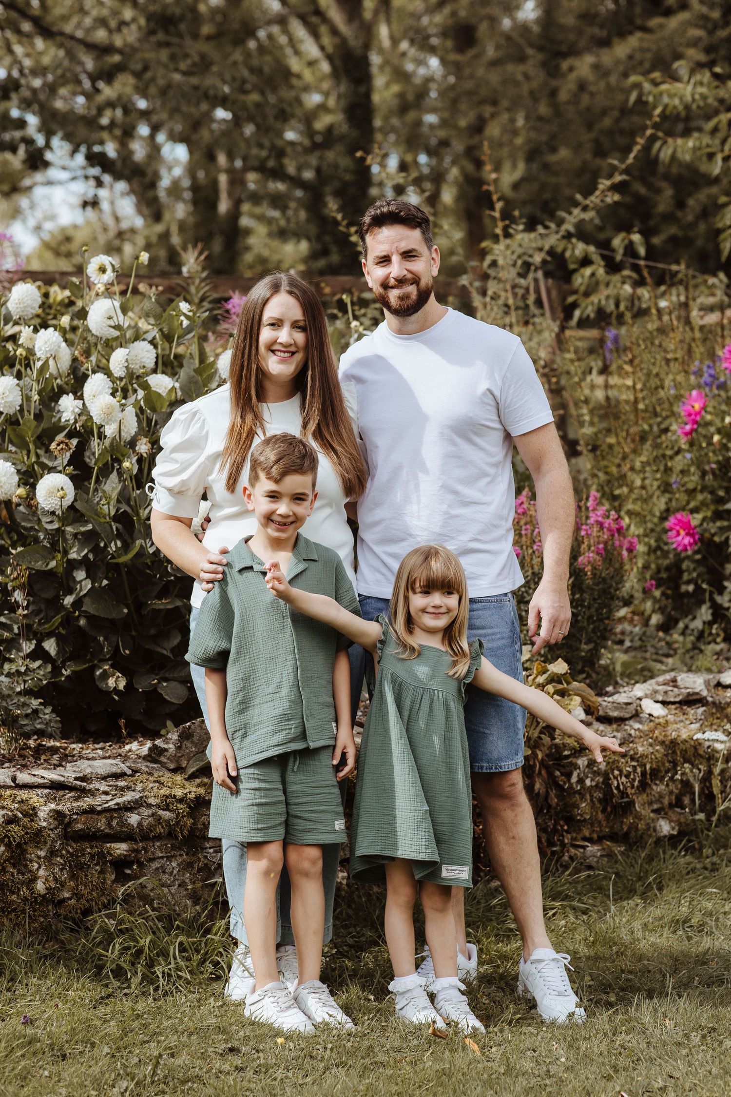 Family of four in coordinated outfits posing in a flower garden during an outdoor photoshoot in Gloucestershire.