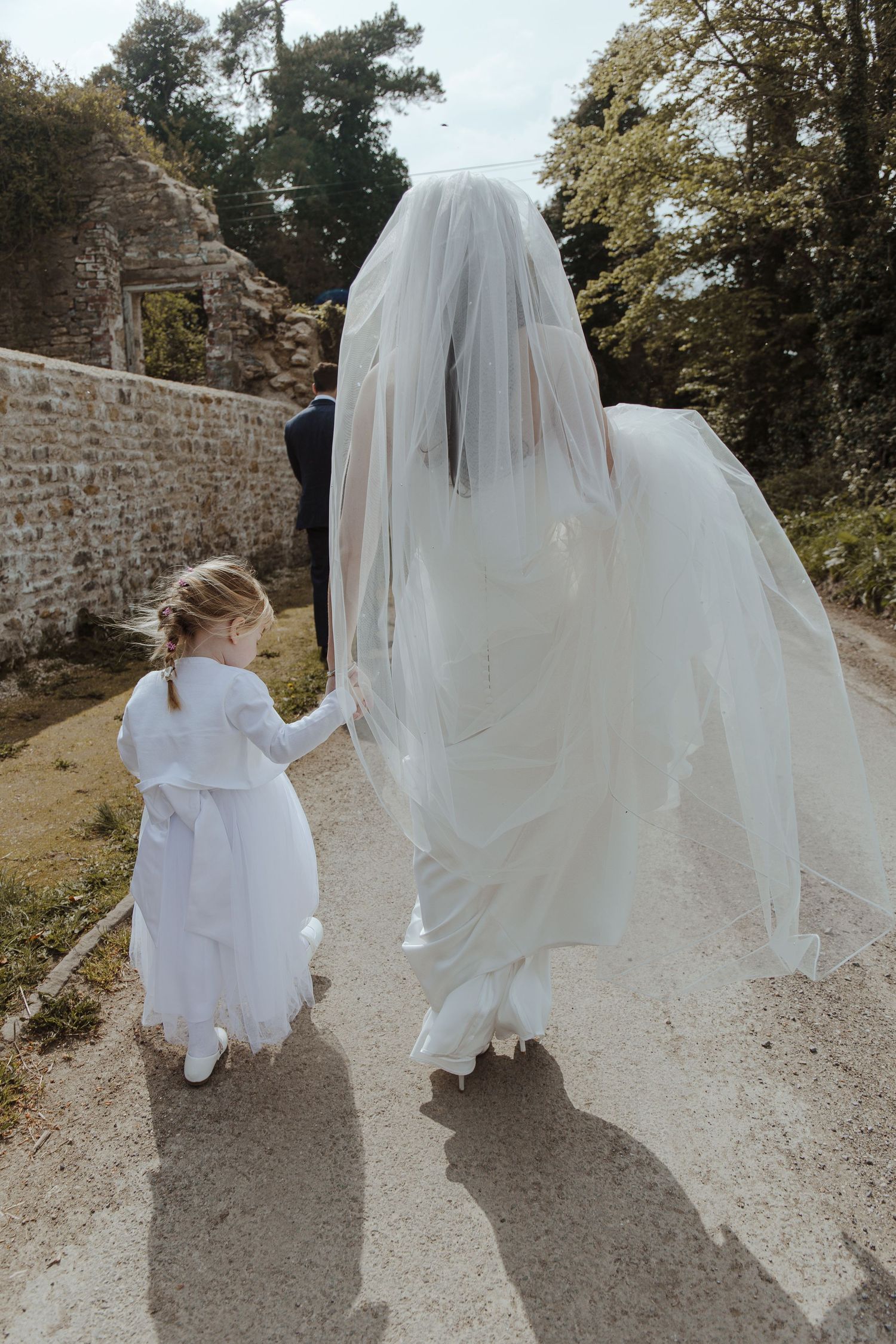 bride walking down a country lane holding a Childs hand and her dress