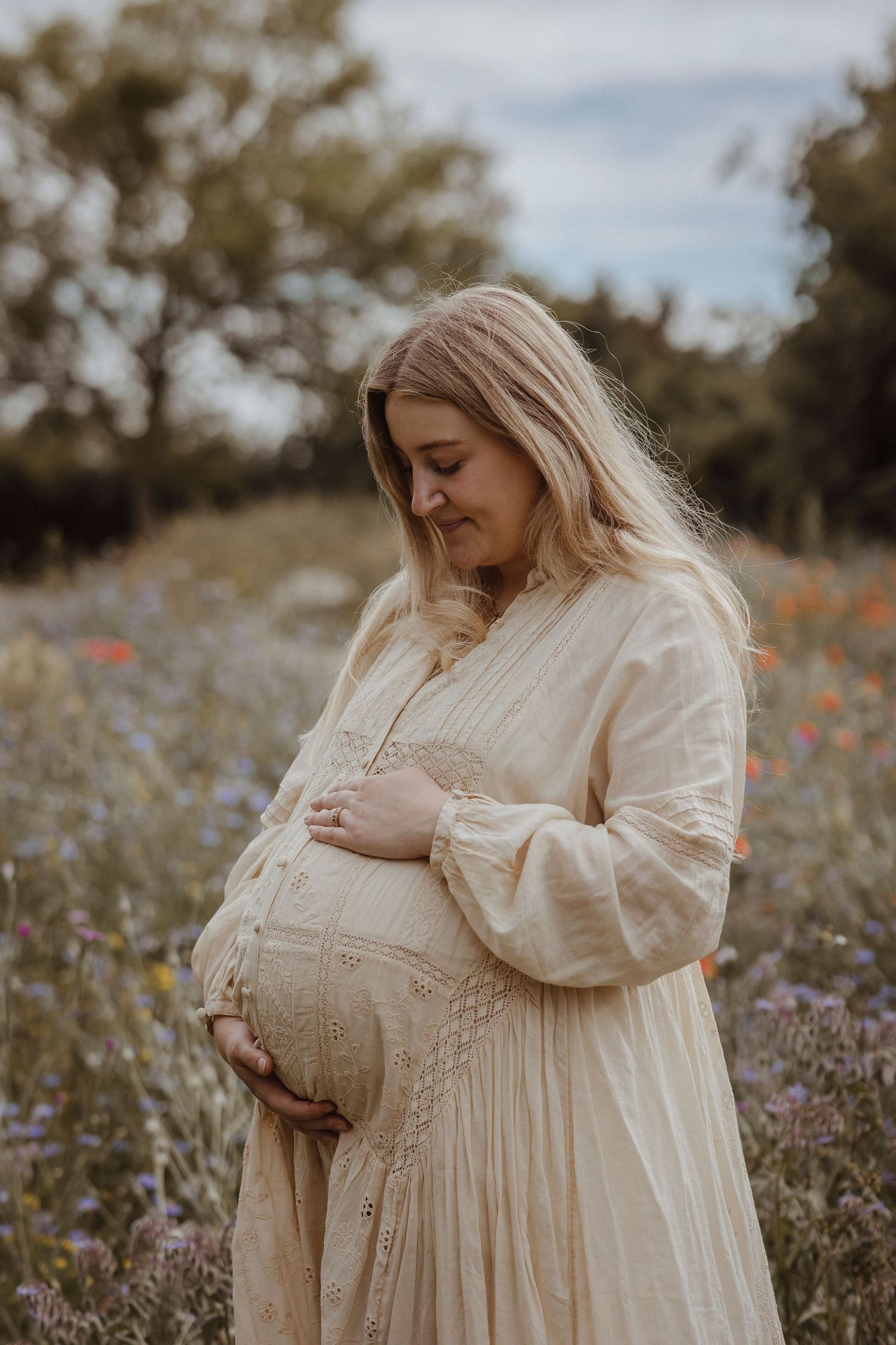 Woman standing holding her bump in a field of wild flowers