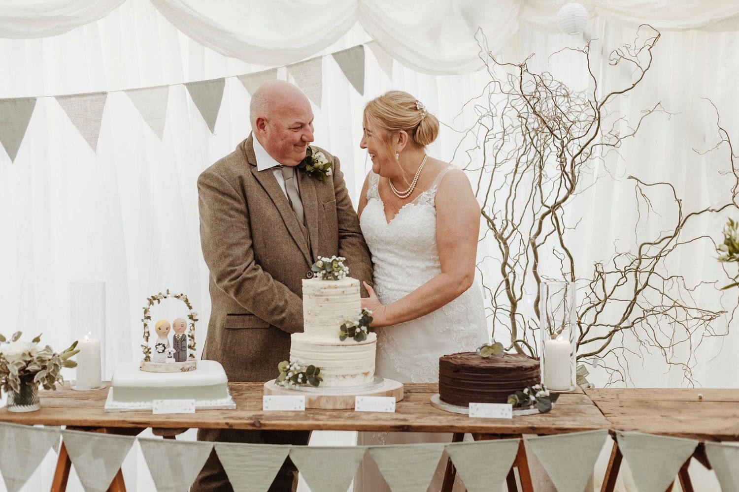 A sweet moment as the couple stands together, hands on the cake, sharing a warm, happy look.
