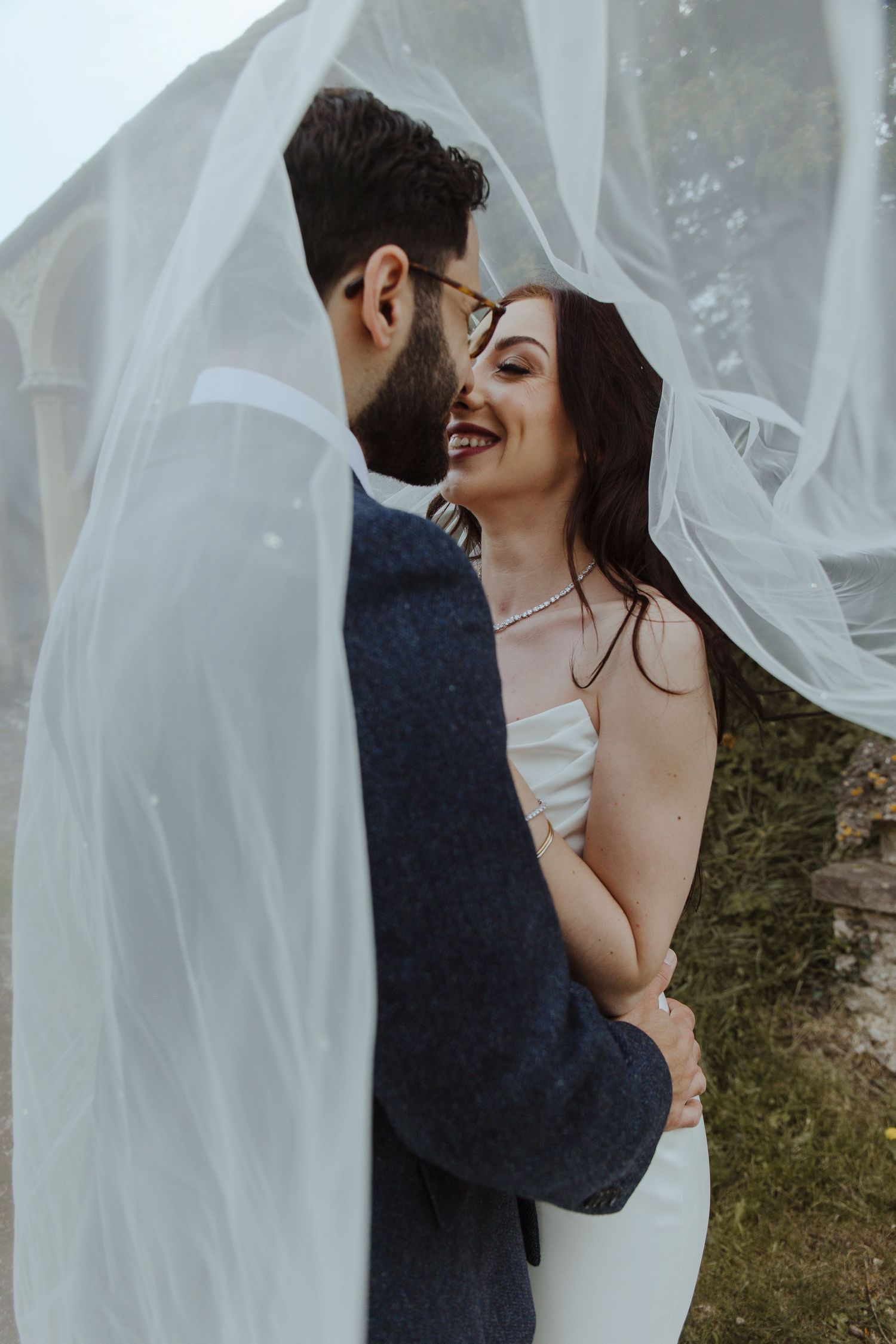 bride and groom standing under her veil laughing