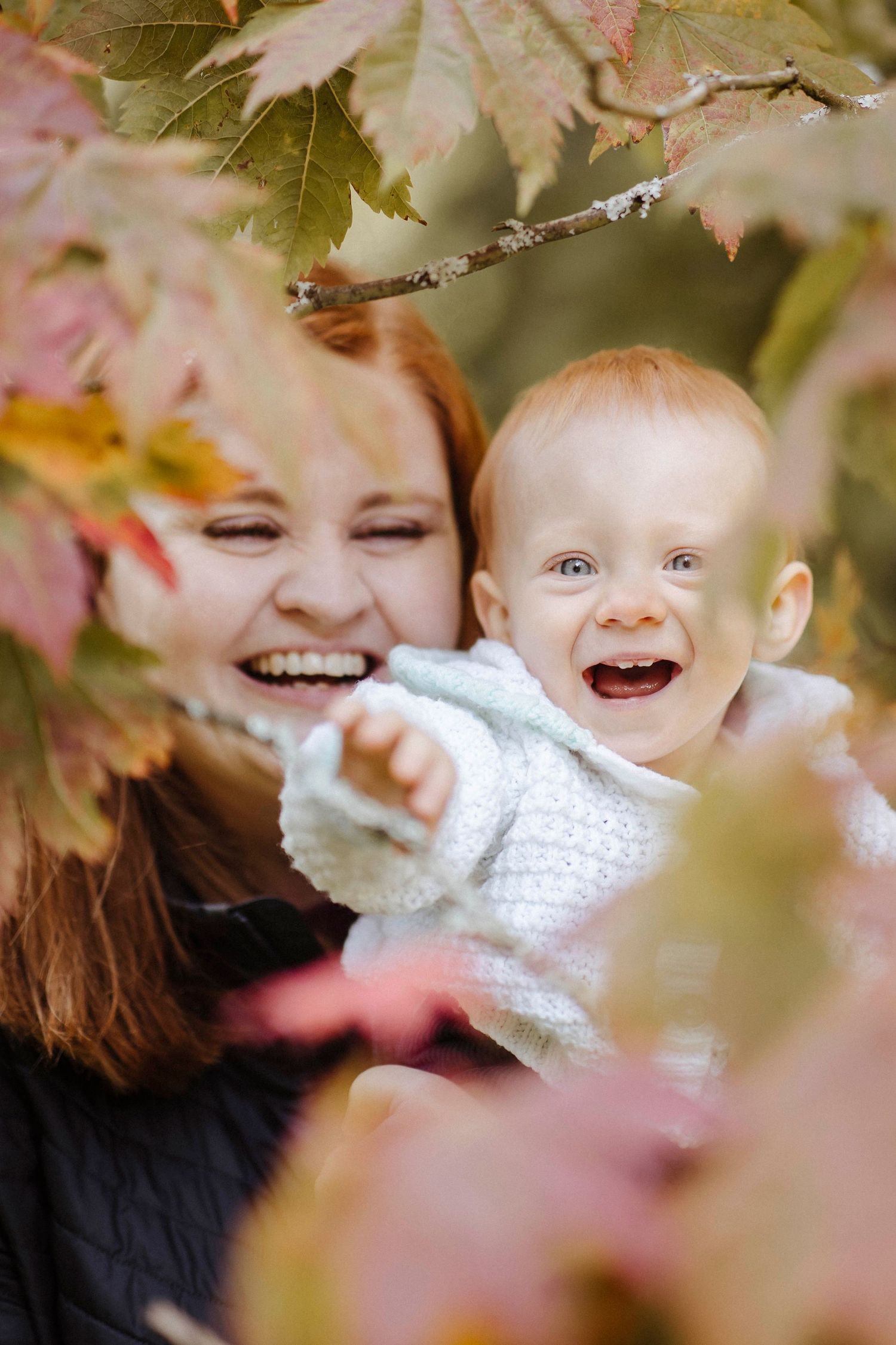 mother and toddler smiling in between the leaves