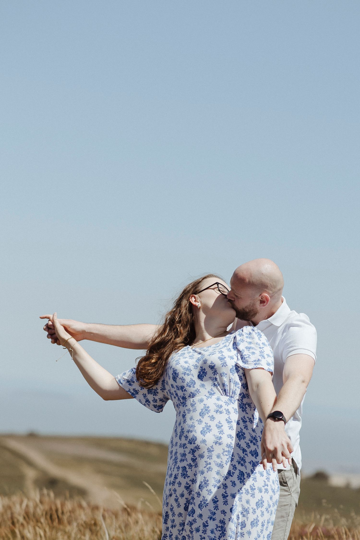 couple kissing in the countrywide whilst holding hands with a blue sky in the background