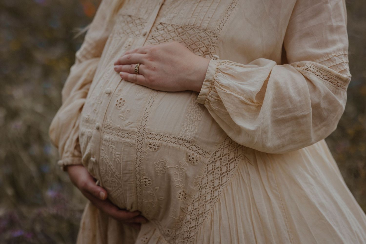Hands rest gently on a flowing dress, highlighting a serene and intimate maternity moment.