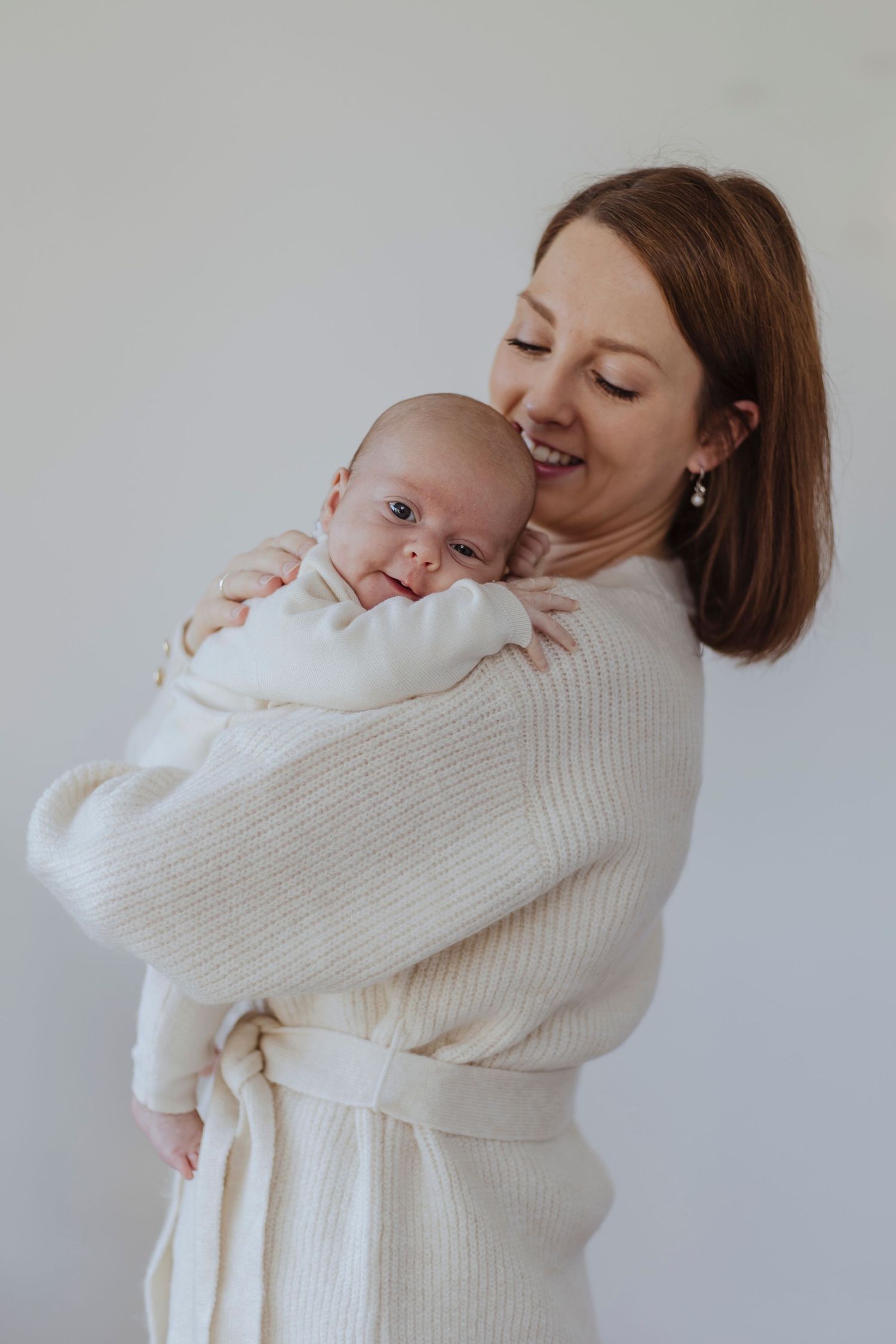 A woman holds a newborn close, smiling softly as the baby rests peacefully against her shoulder.