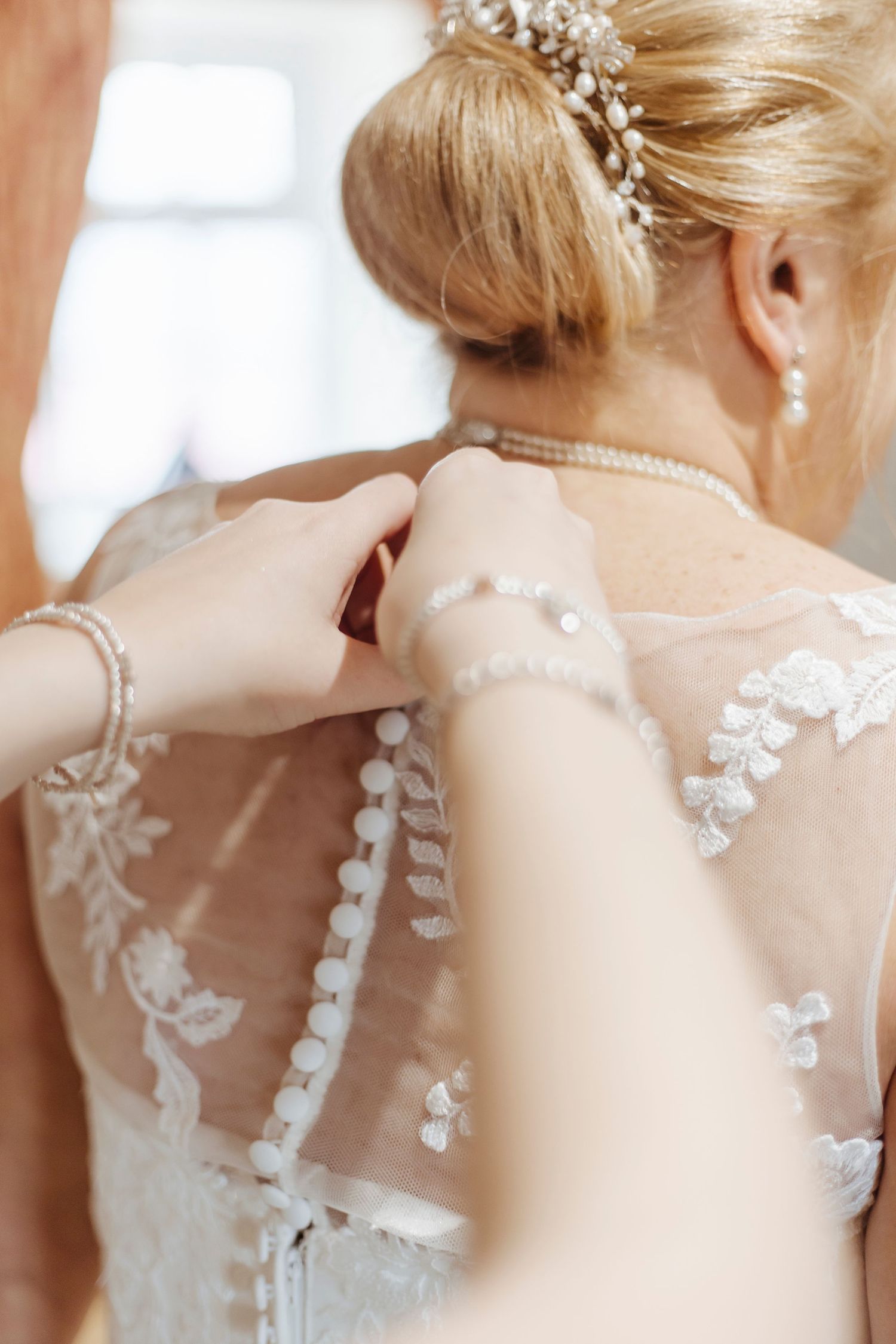 Delicate hands fasten the bride’s intricate buttons—quiet, loving anticipation before the celebration begins.
