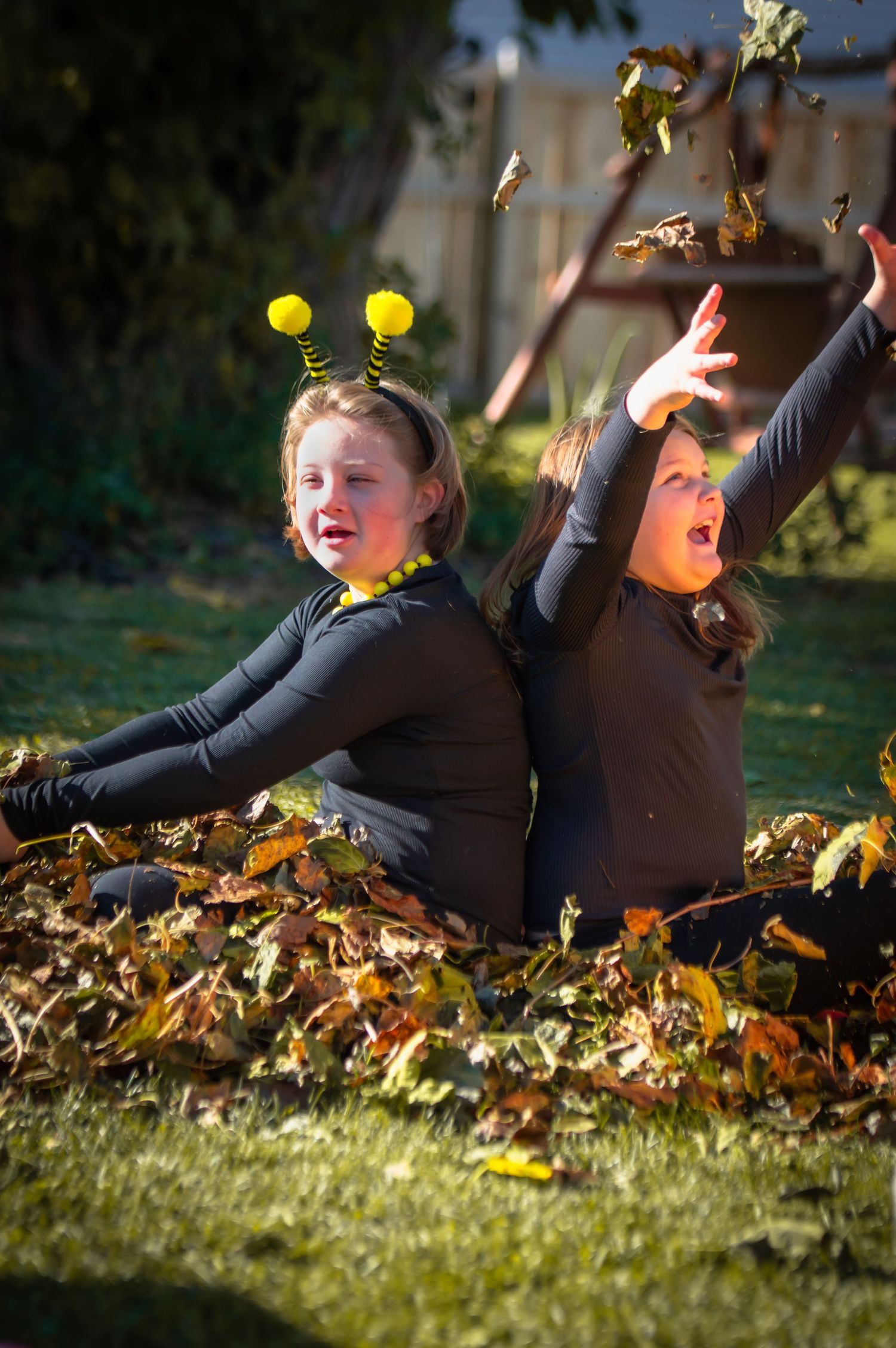 Children playing joyfully in pile of autumn leaves on sunny day.