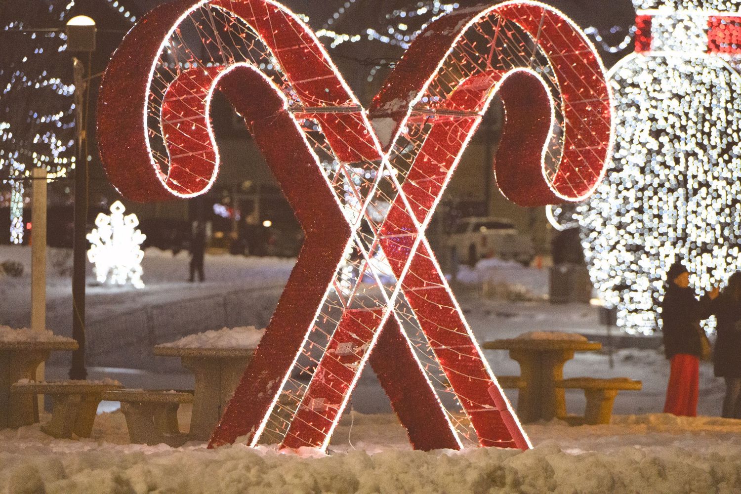 Holiday decorations featuring large red and white candy canes and twinkling lights illuminate an outdoor shopping area at night.
