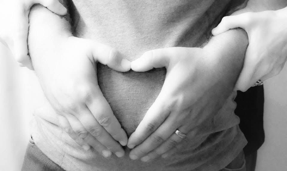 Black and white close-up of hands forming a heart shape over a person's torso.