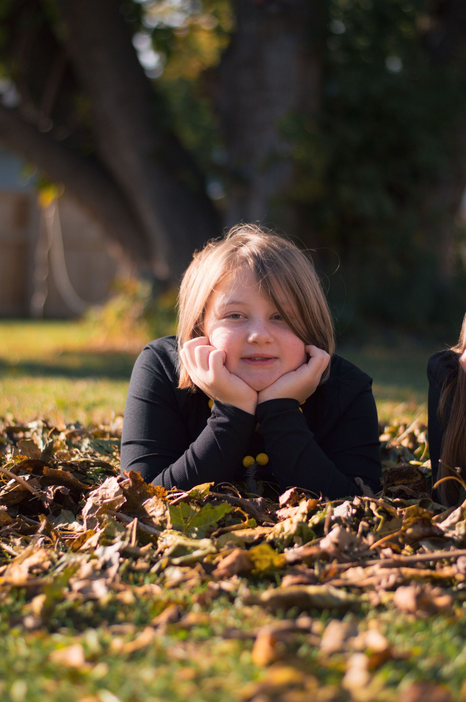 Child resting on fallen autumn leaves during outdoor portrait session.