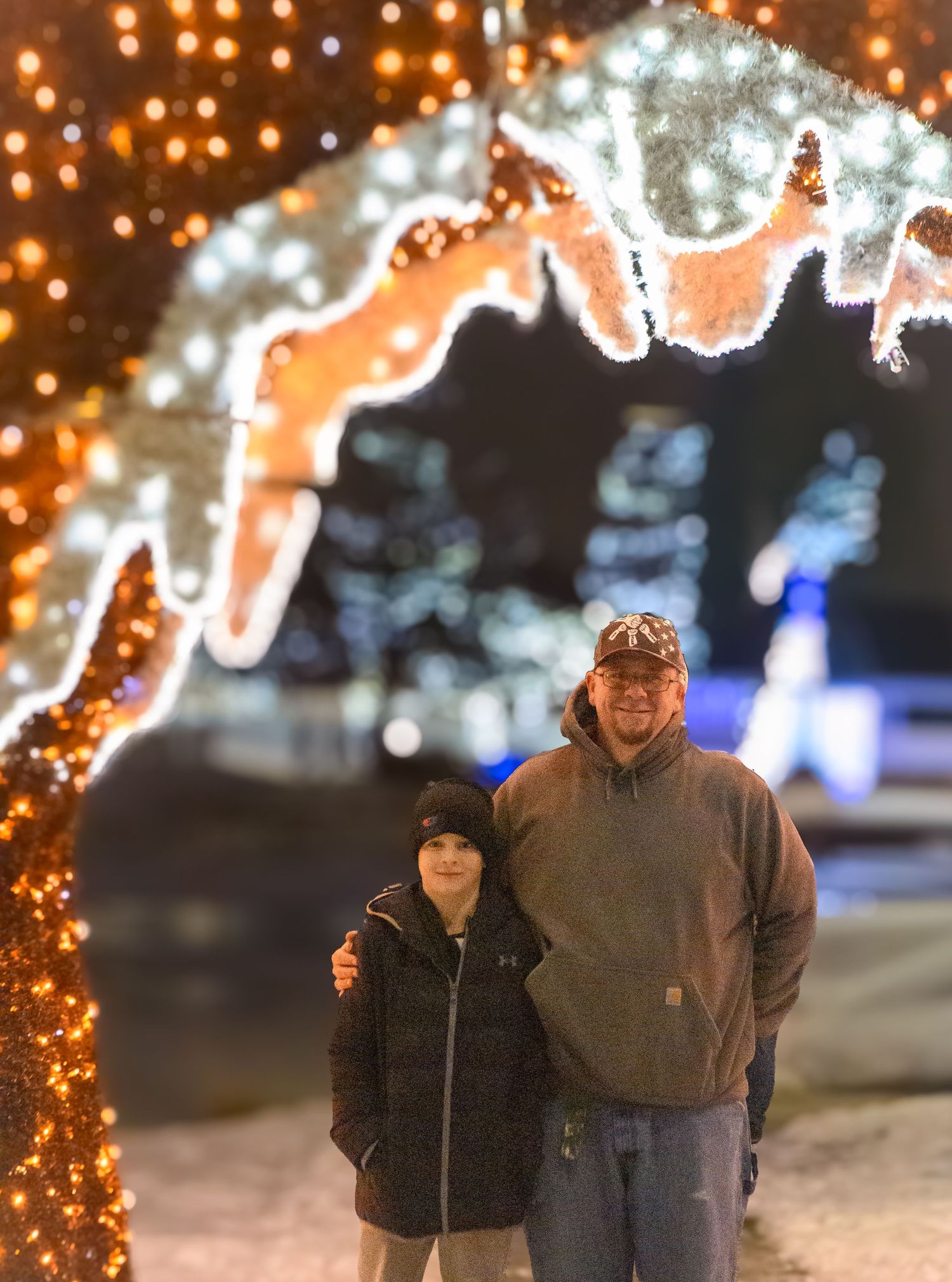Two people walk along an illuminated winter path with glowing archways and holiday lights creating a magical atmosphere.