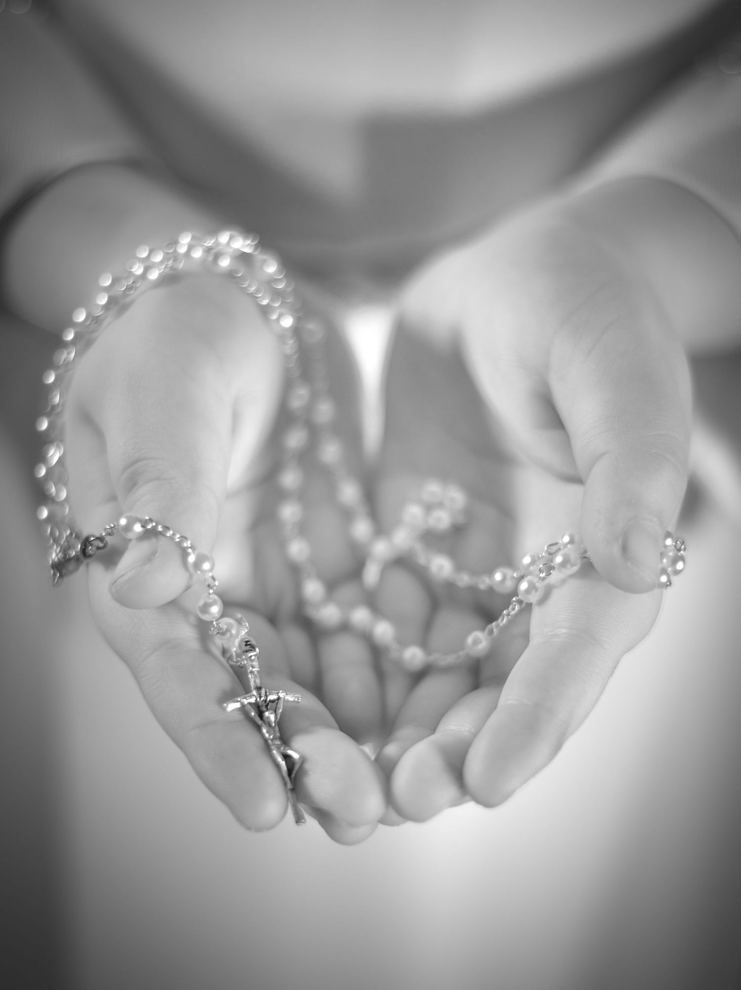 A pair of hands gently cradles a delicate silver tiara adorned with crystals in a dreamy black and white photograph.