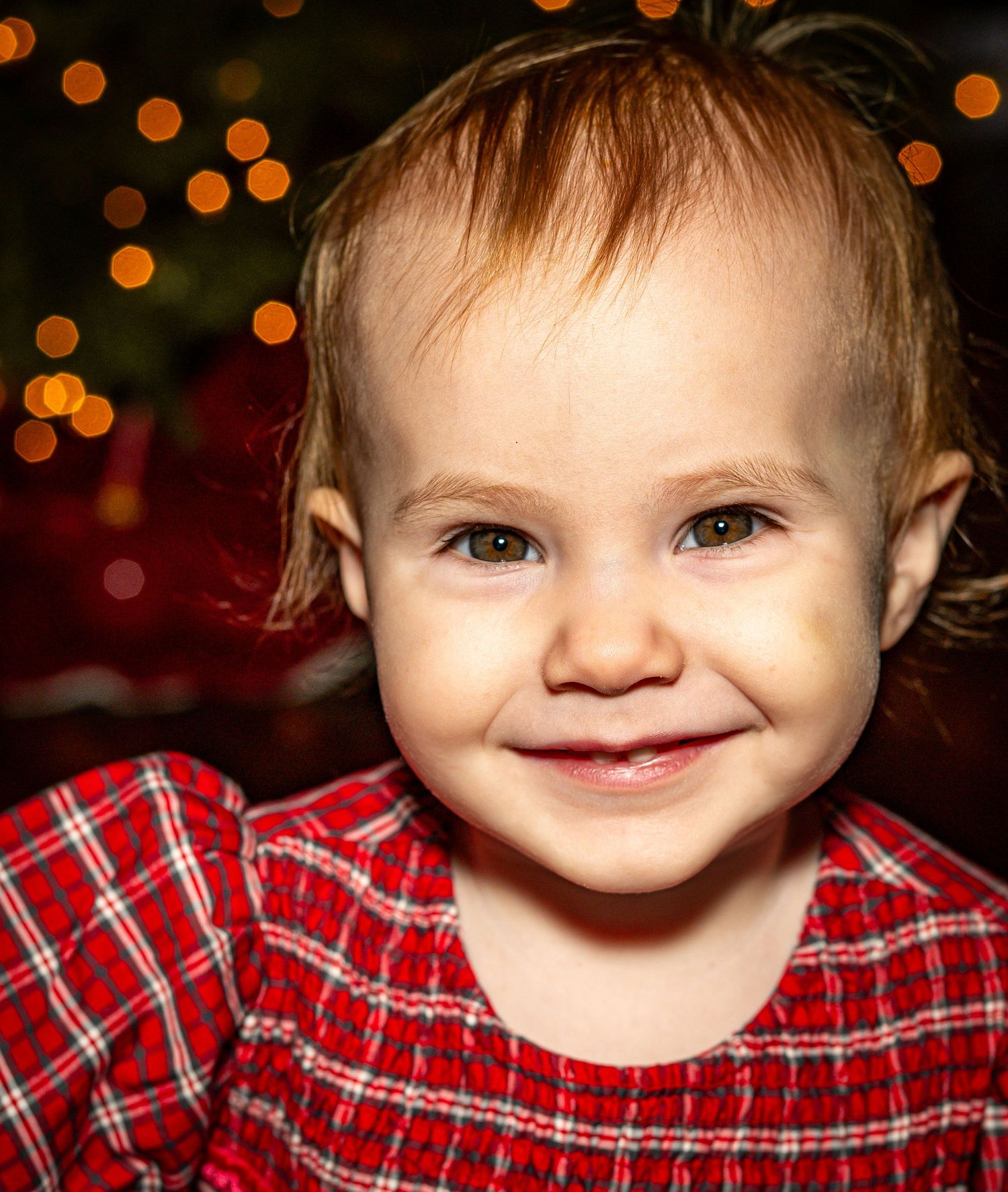 A smiling child in a red plaid shirt shown in a series of close-up shots with warm bokeh lighting in the background.