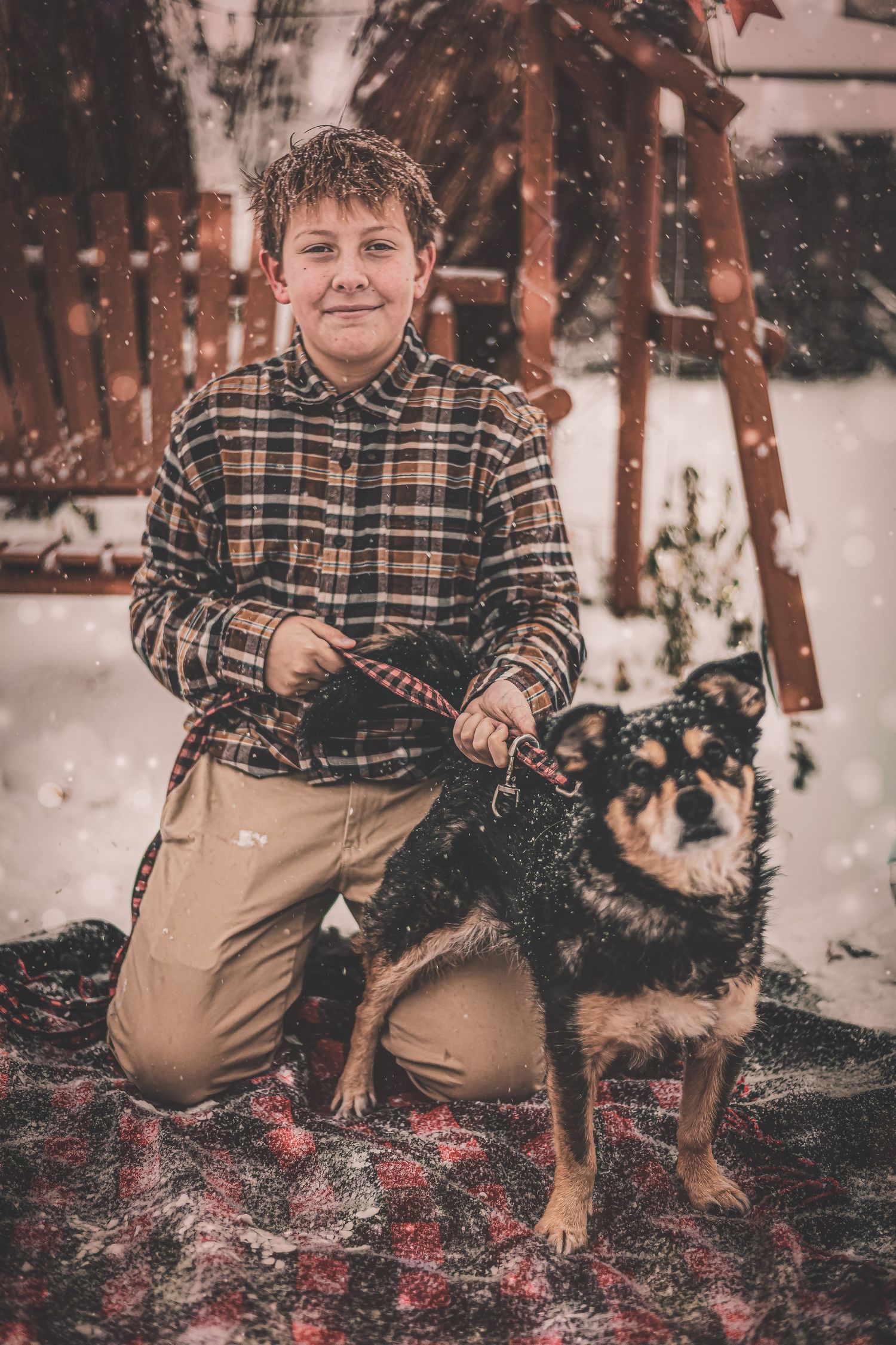 Person in plaid shirt kneeling next to a German Shepherd mix dog in snowy winter setting.