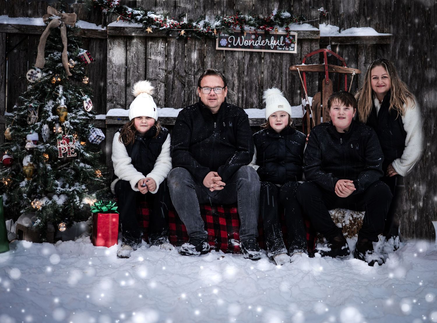 A group sits together on snowy steps wearing winter clothing and buffalo plaid patterns in a festive outdoor setting.