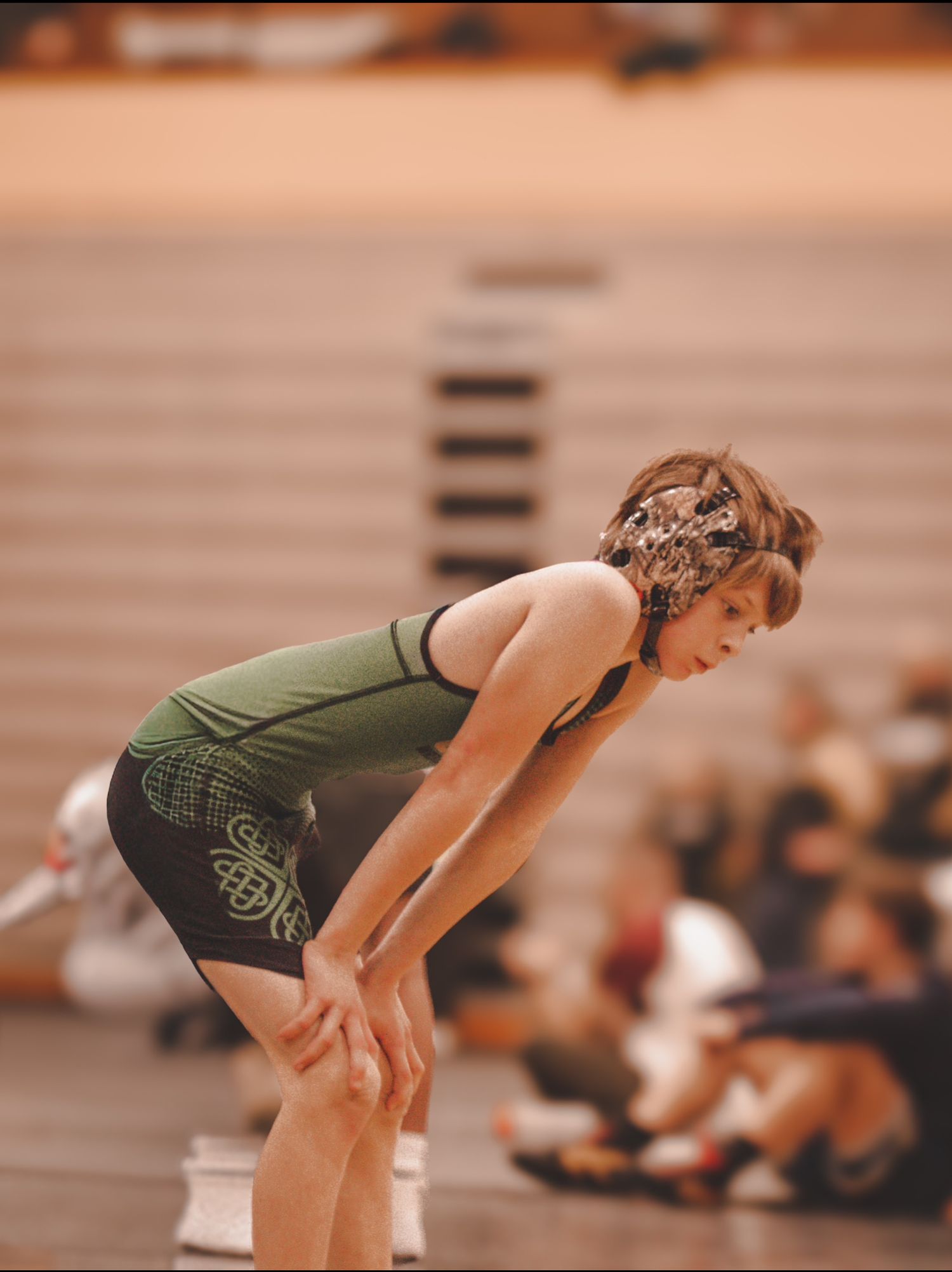 Athlete in green uniform rests between plays during an intense sports match with hands on knees.