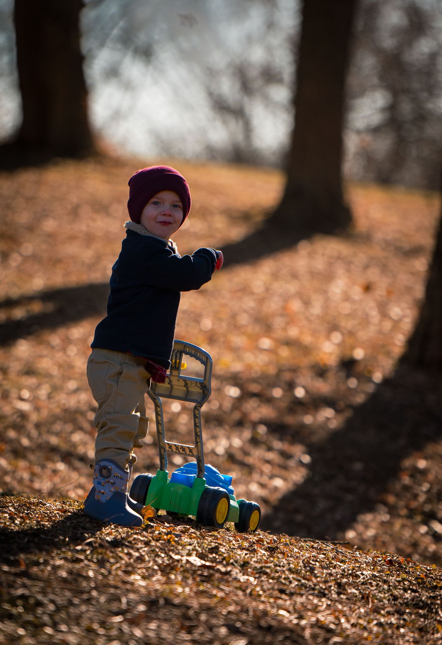 A child plays with a colorful toy truck in autumn leaves on a sunny day in the park.