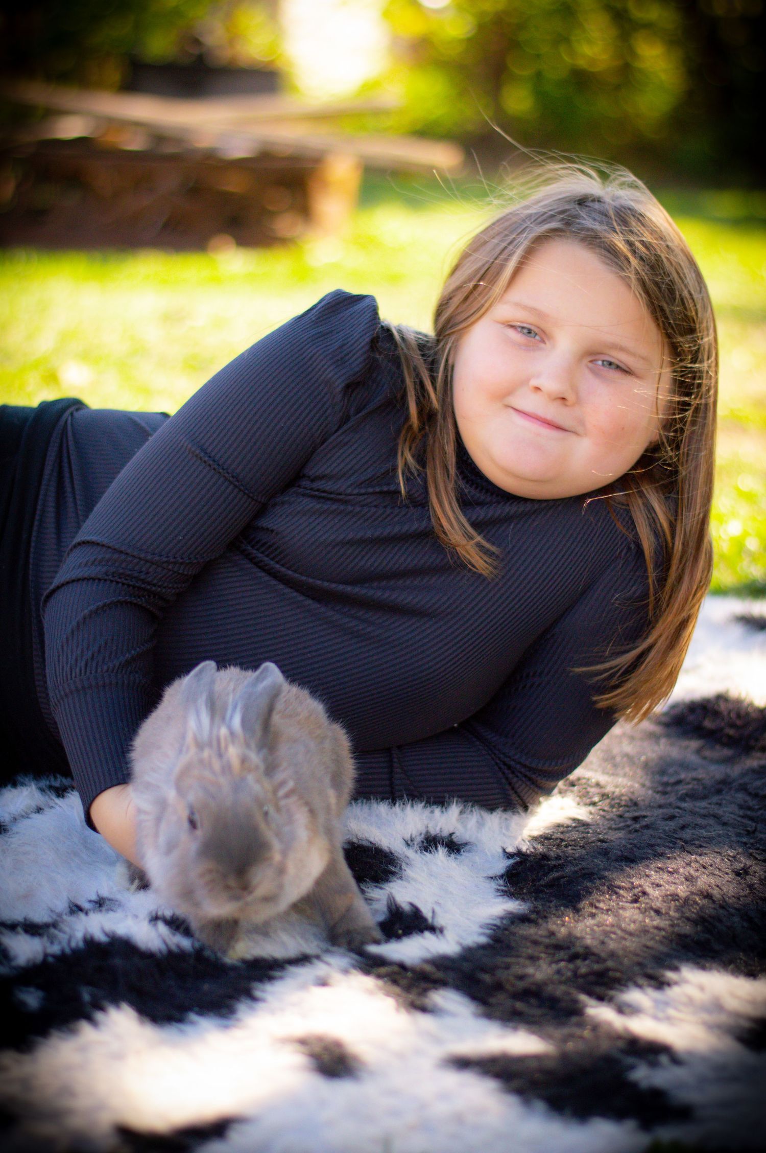 Candid outdoor portrait lying on black and white fur in sunlit setting.