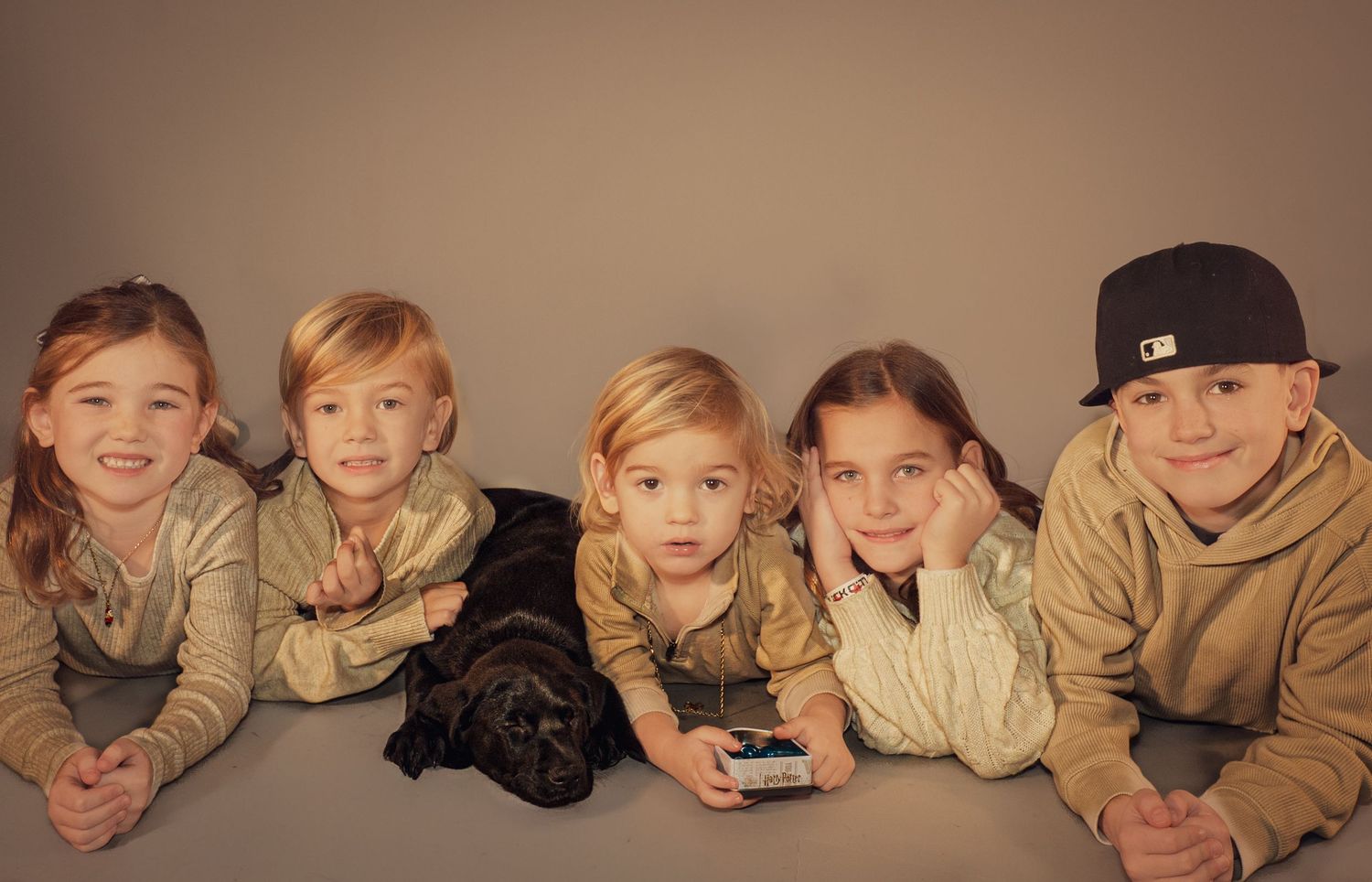 A panoramic group photo of children lying on their stomachs in a row wearing casual clothing.