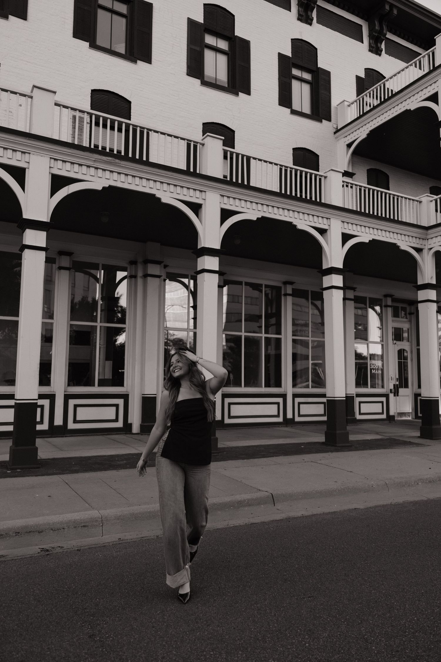 Black and white photo of a woman posing in front of a historic building with arched columns and balcony.
