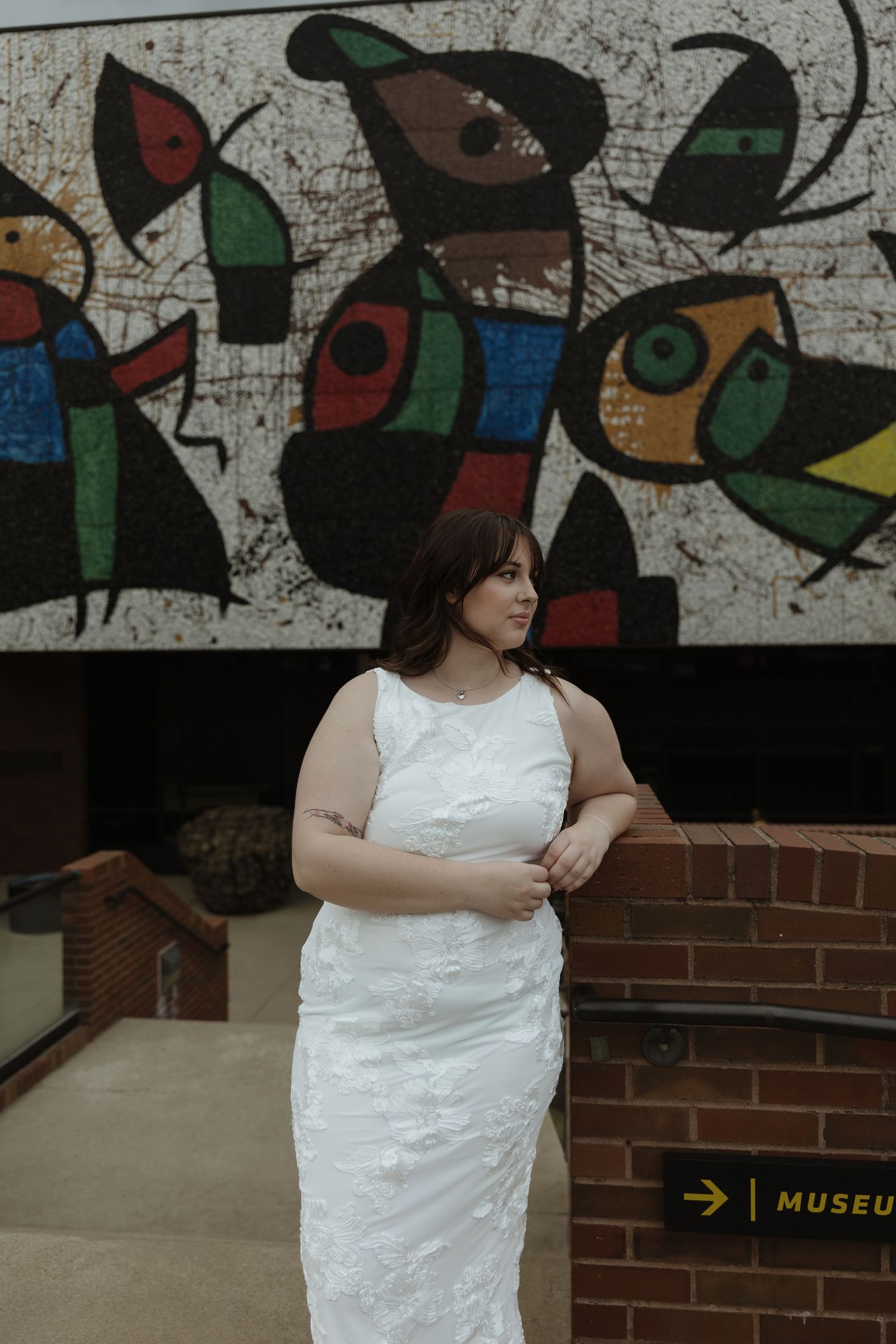 Bride in white lace dress poses in front of colorful Joan Miro mural outside a museum.