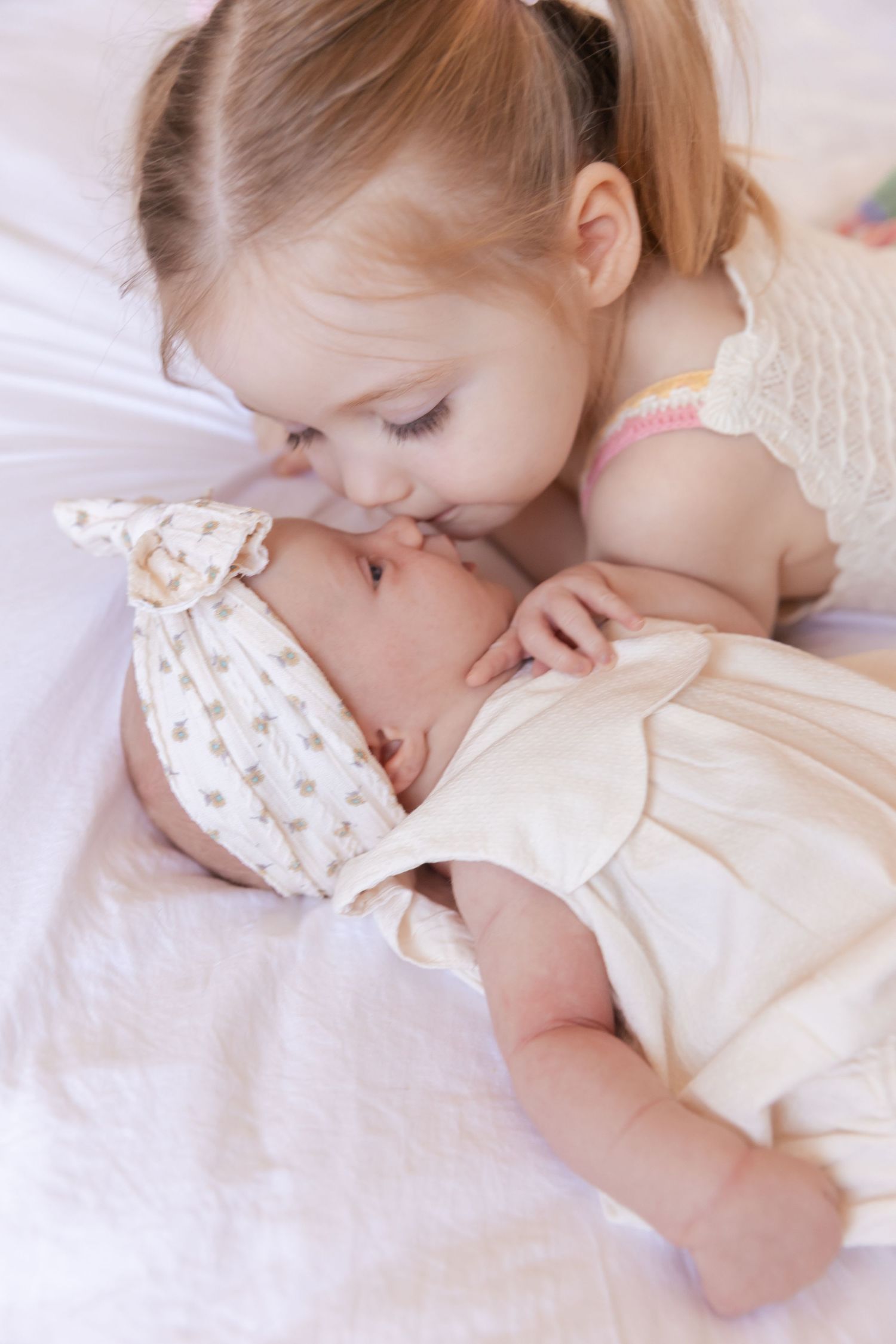 newborn baby girl with big sister giving her a kiss on her nose