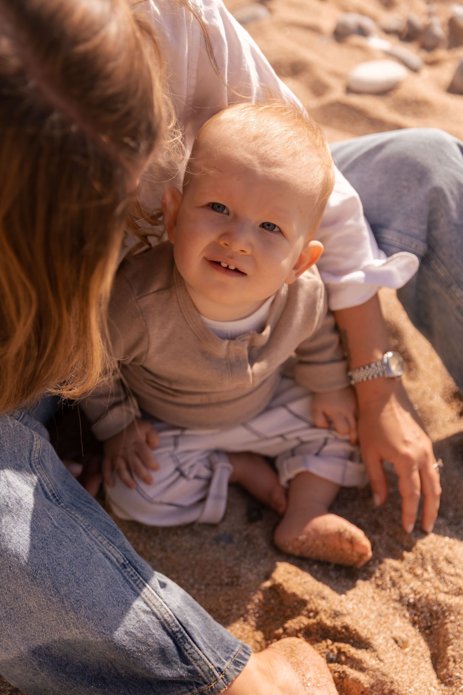 young boy smiling at the camera sitting in between mothers legs on eastbourne beach