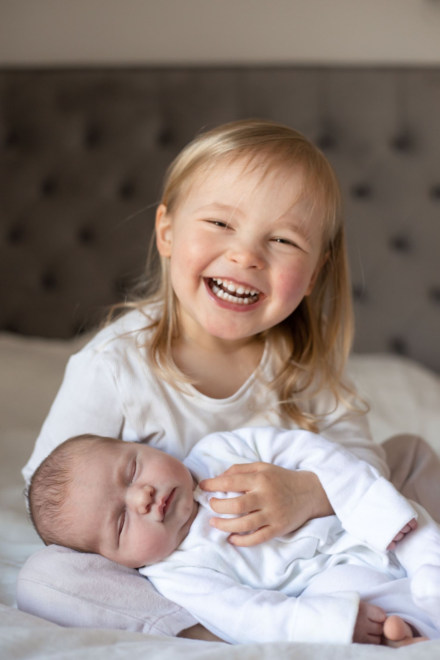 young girl smiling and newborn baby sister in her arms
