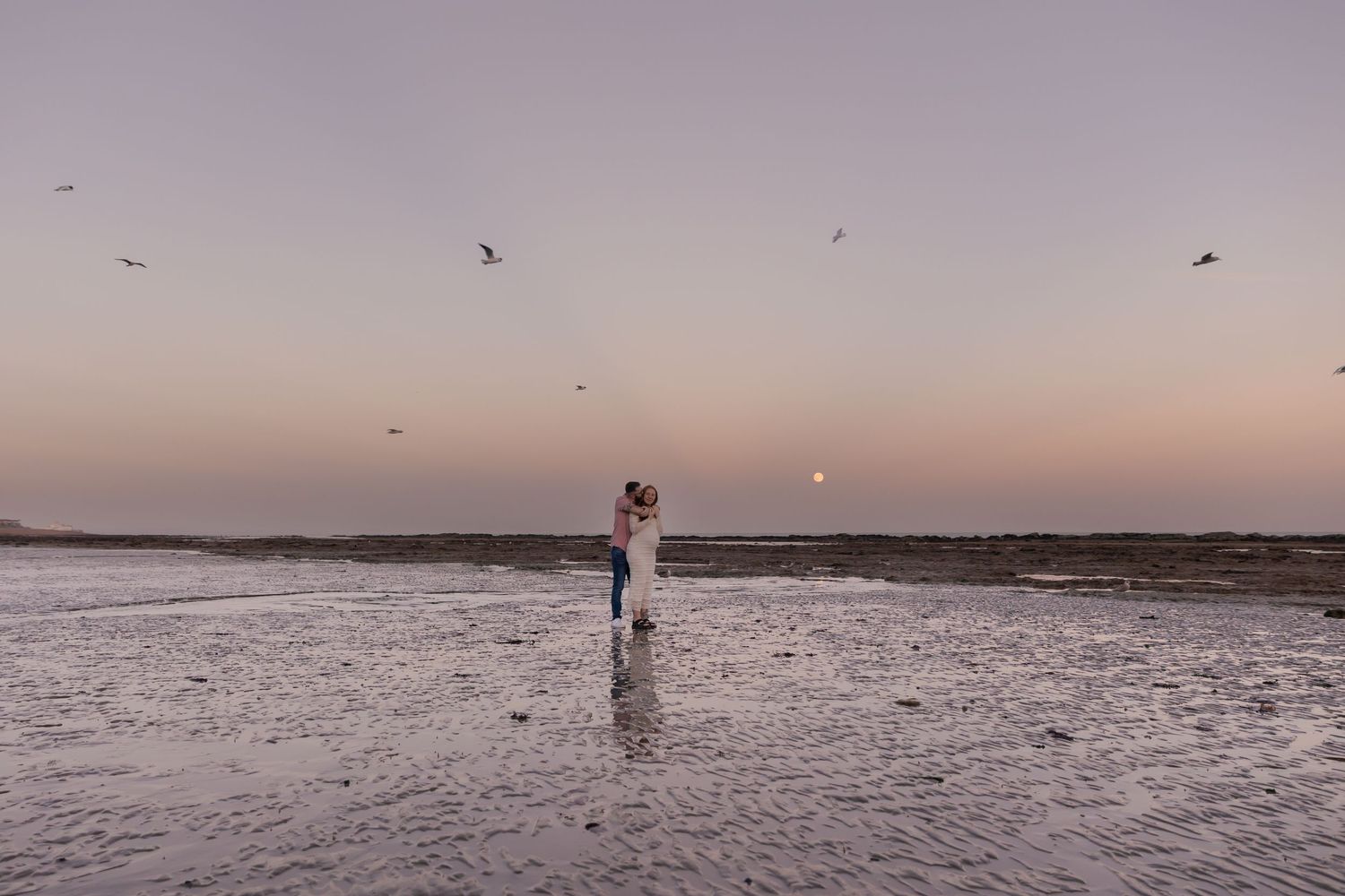 a pregnant mother and her partner during a maternity photoshoot at sunset on eastbourne beach