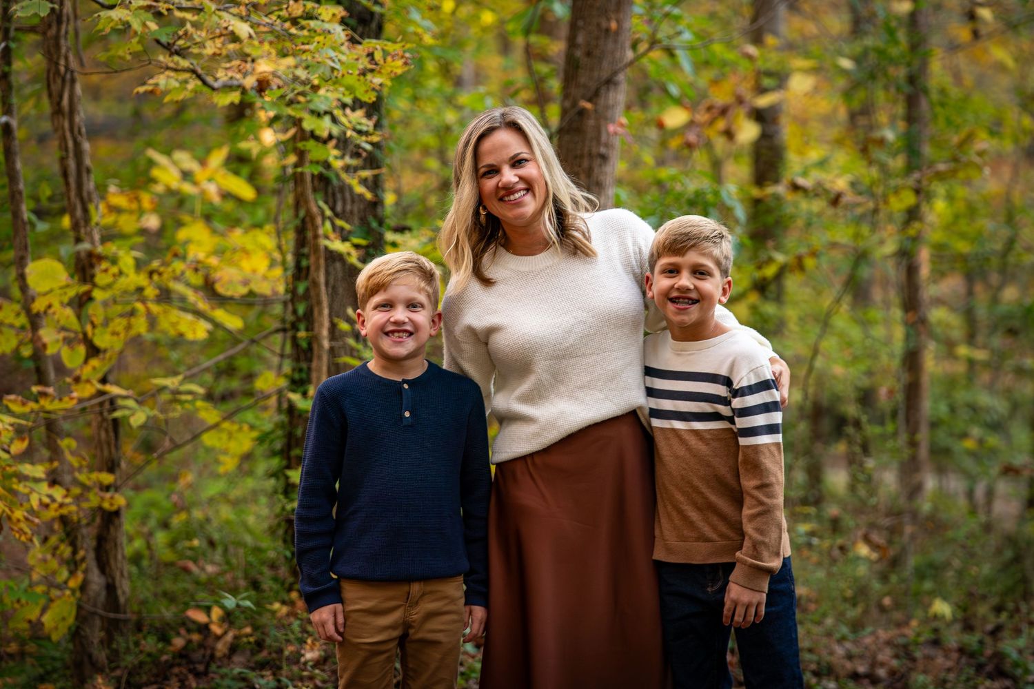 Family portrait with coordinating earth-tone outfits against a backdrop of fall trees.