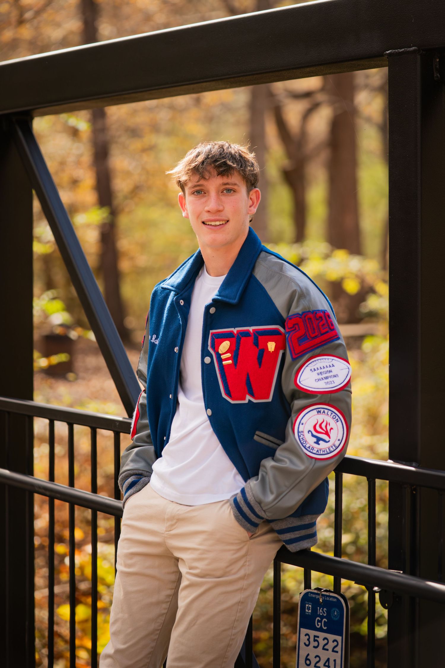 Student wearing a varsity letterman jacket poses on outdoor steps during autumn.
