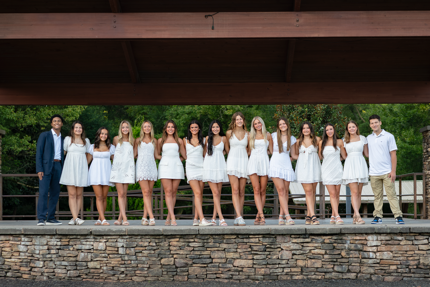 Students arranged in casual poses along stone wall for outdoor group portrait.