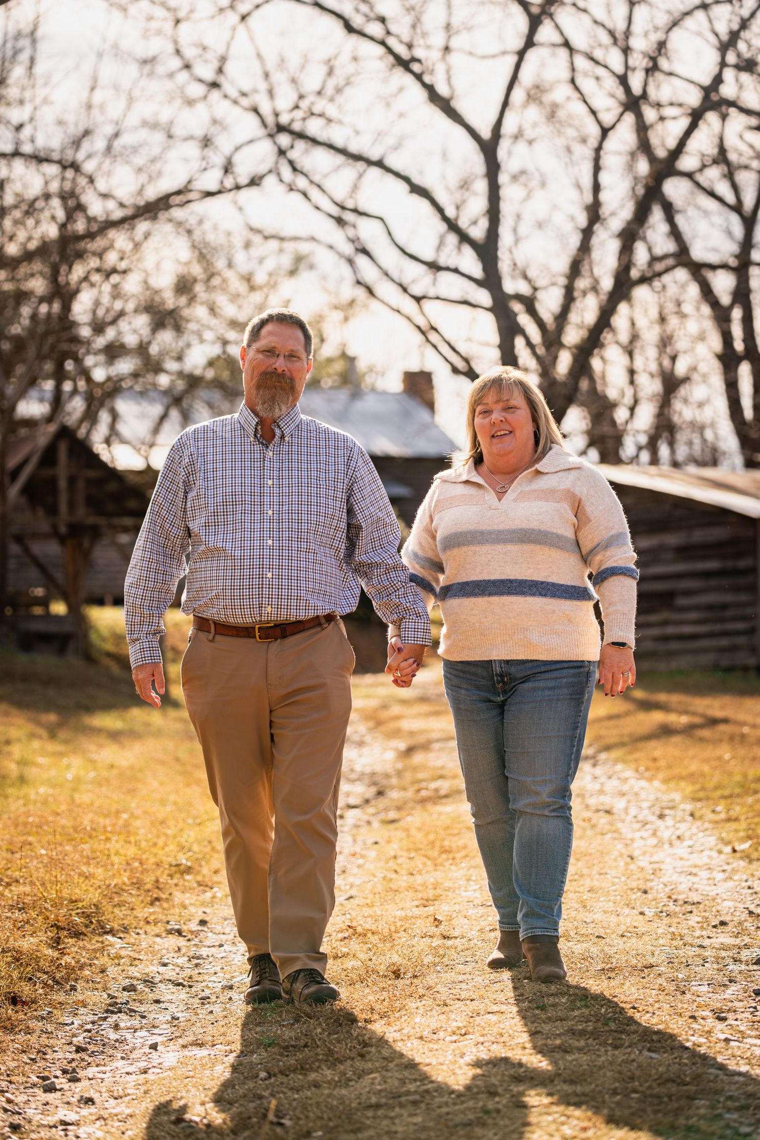 A couple walks hand in hand on a sunlit autumn path through a park at golden hour.